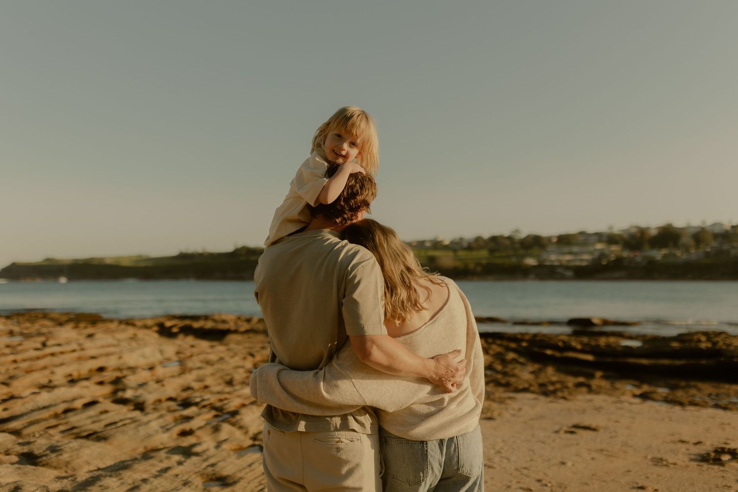A family shares a warm embrace on a sandy beach during a beautiful golden sunset.
