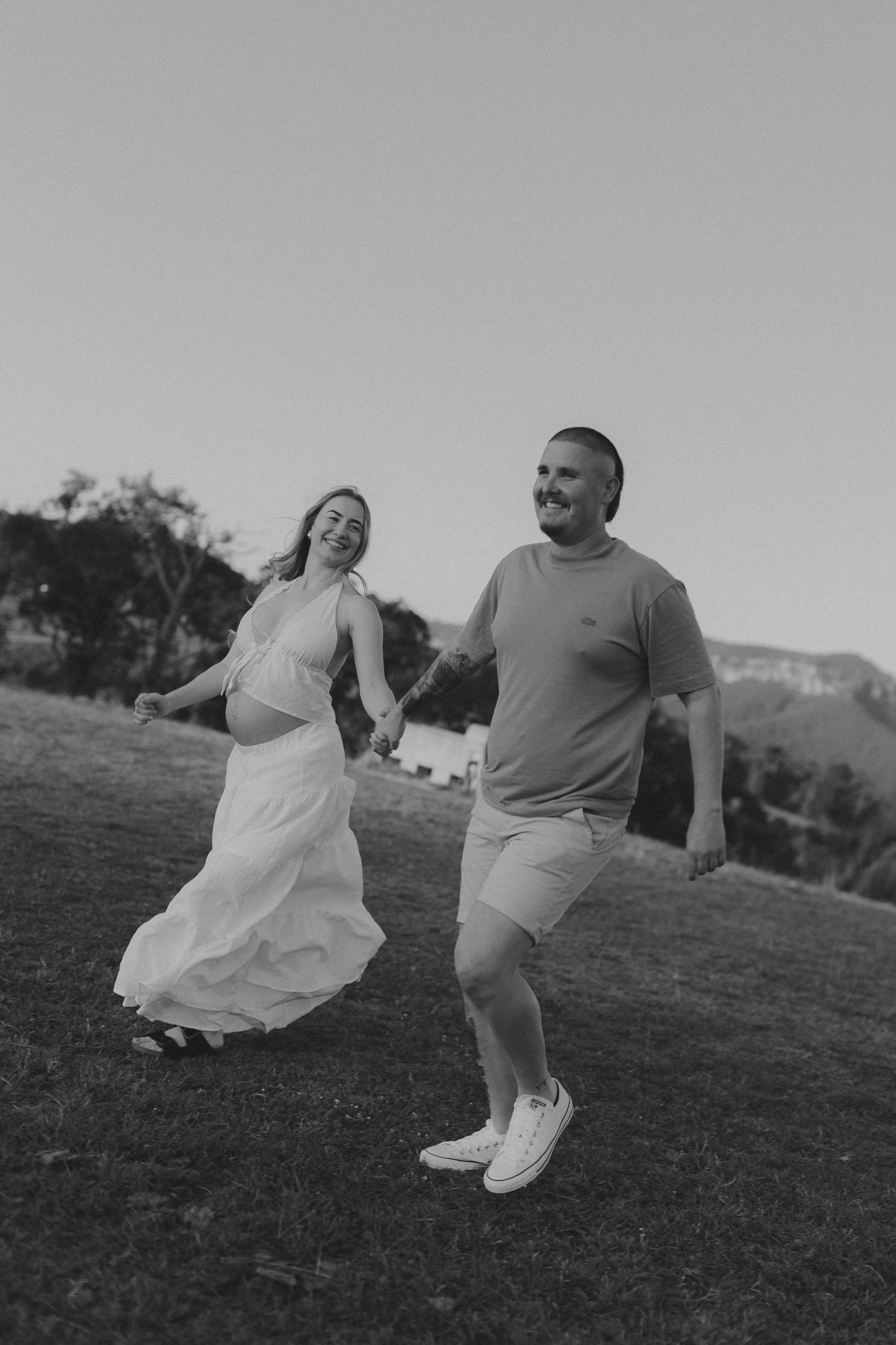 Black and white photo of happy couple holding hands and running together in open field.