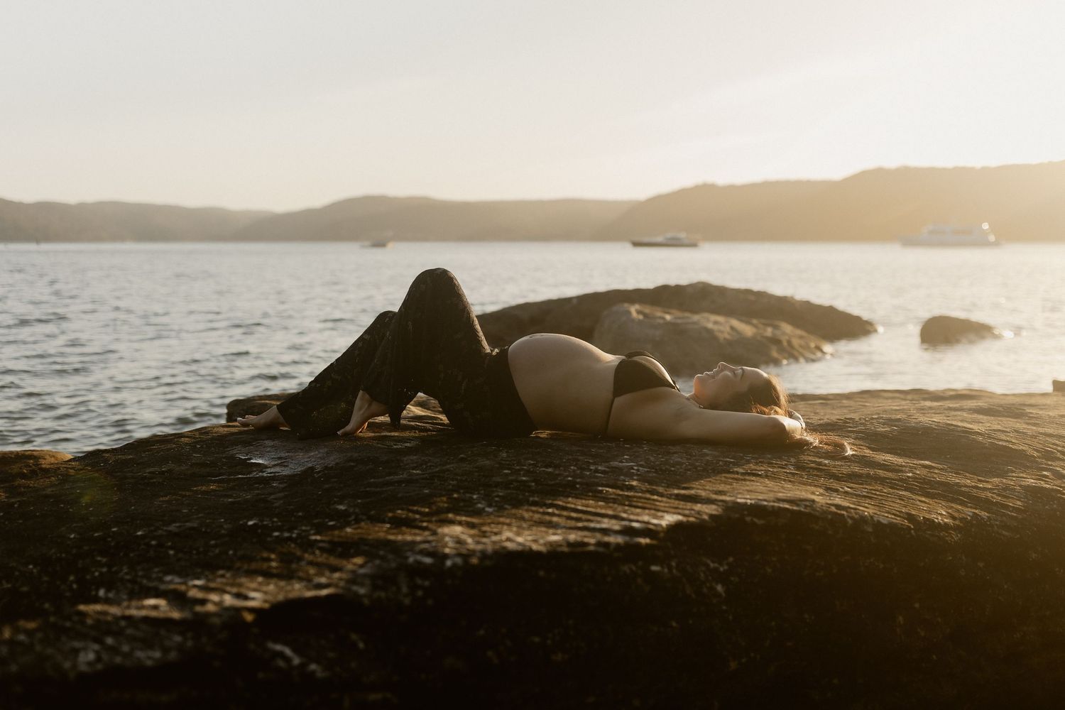 Silhouetted figures standing on rocky coastline at sunset with dramatic golden light over ocean waves.
