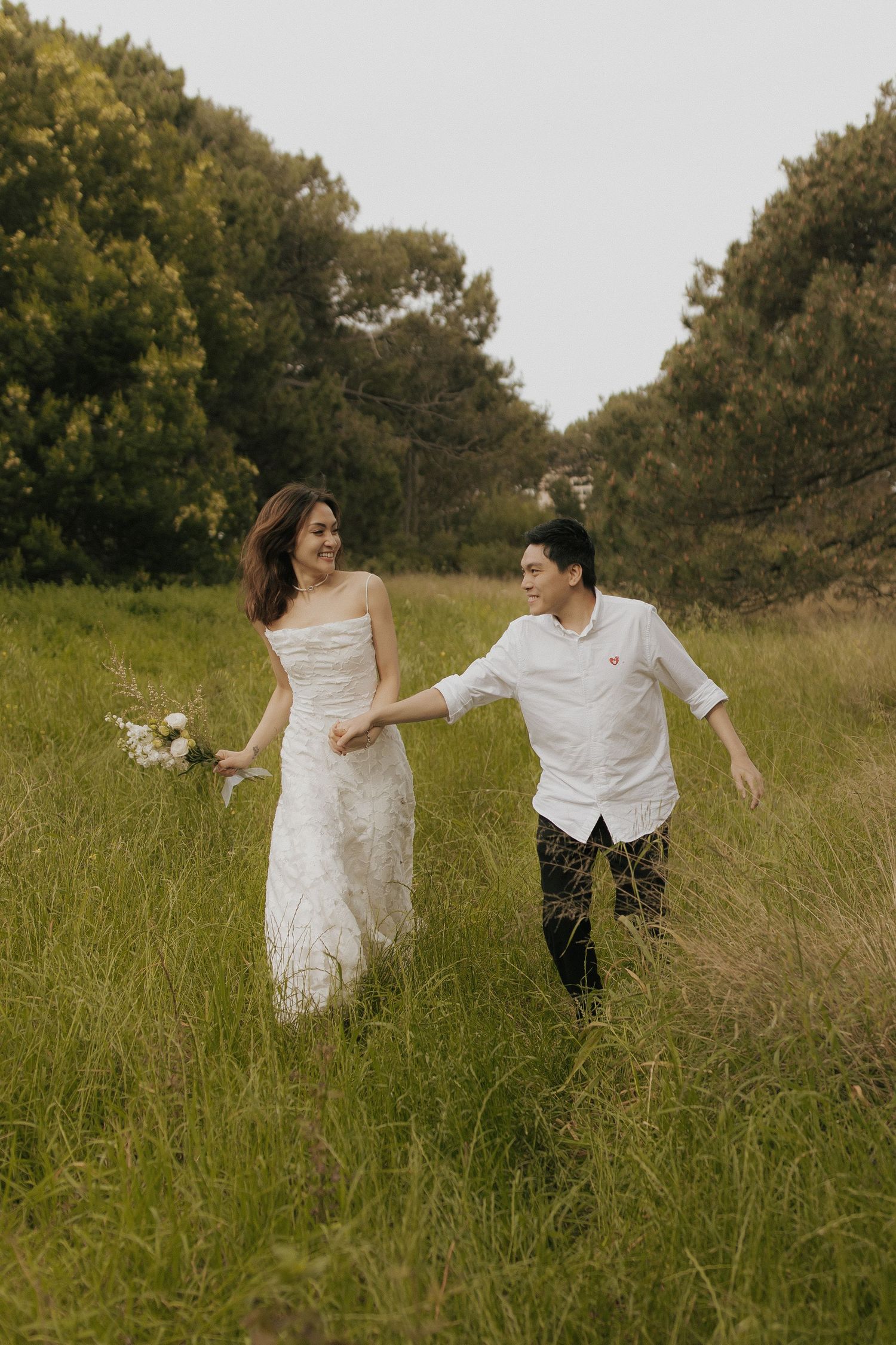 A couple runs joyfully through a meadow of tall grass during a photo session.