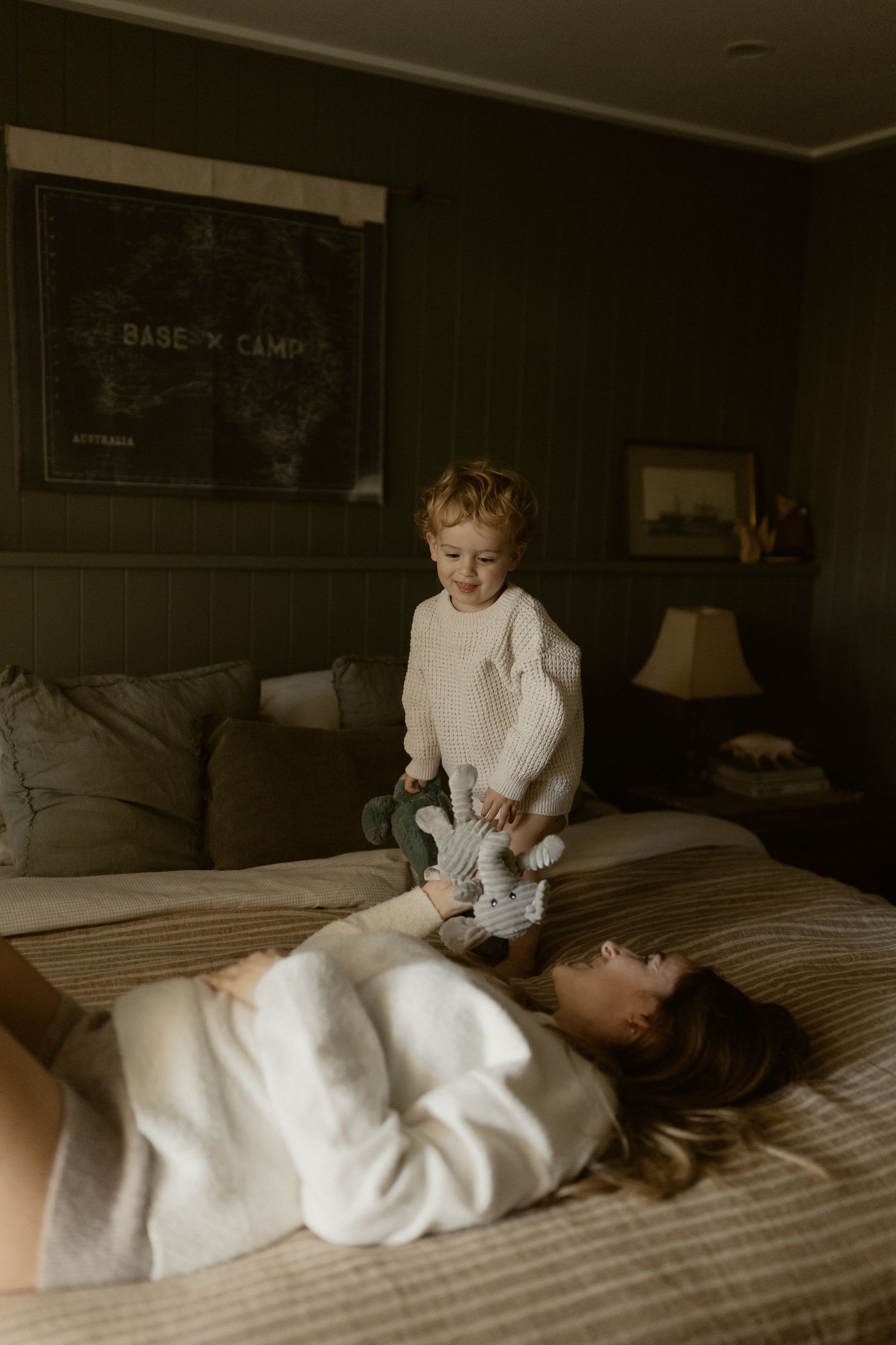 A cozy indoor scene with white bedding and soft natural lighting shows playtime between two figures.