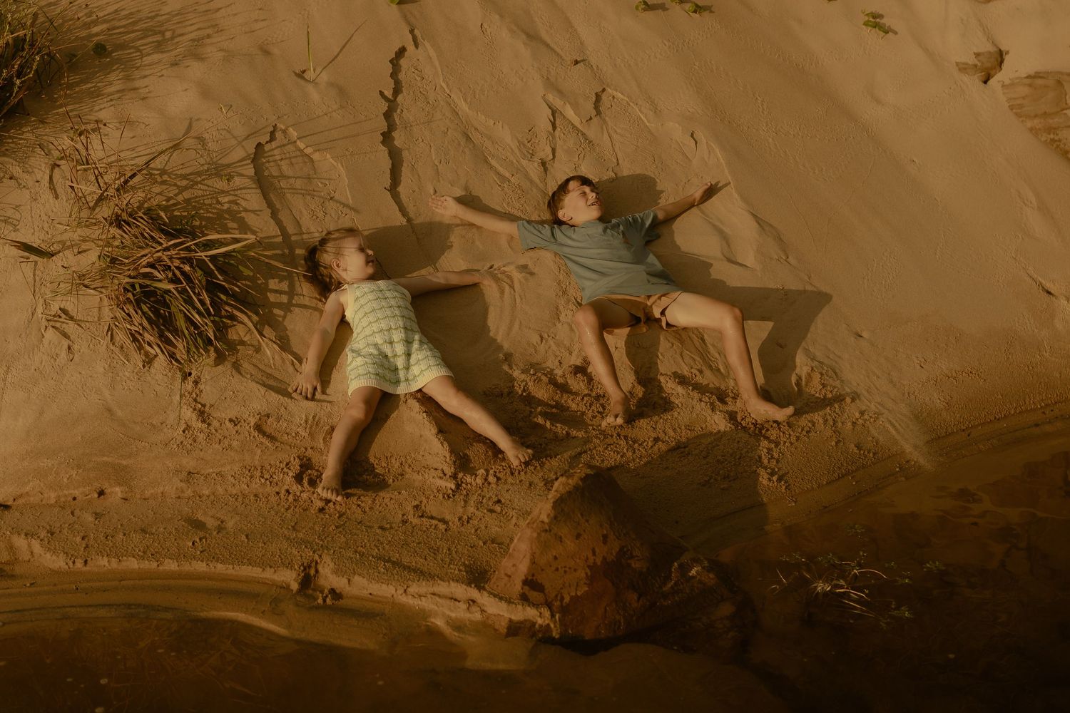 Kids slide down sandy dunes at the beach during golden hour.