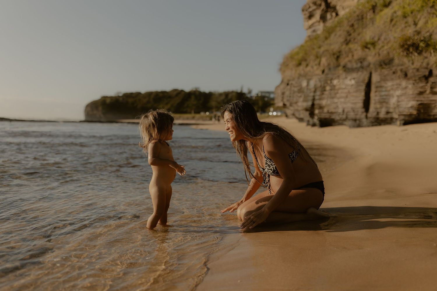 Beachgoers relax and play near the shoreline as waves roll in during golden hour.