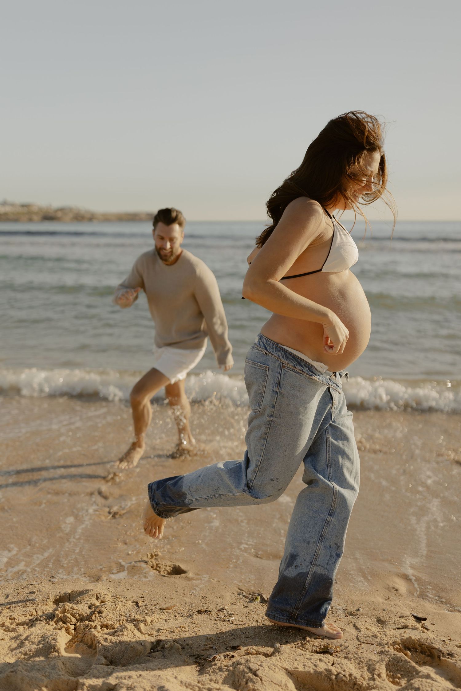 Playful couple running and splashing in ocean waves at beach.
