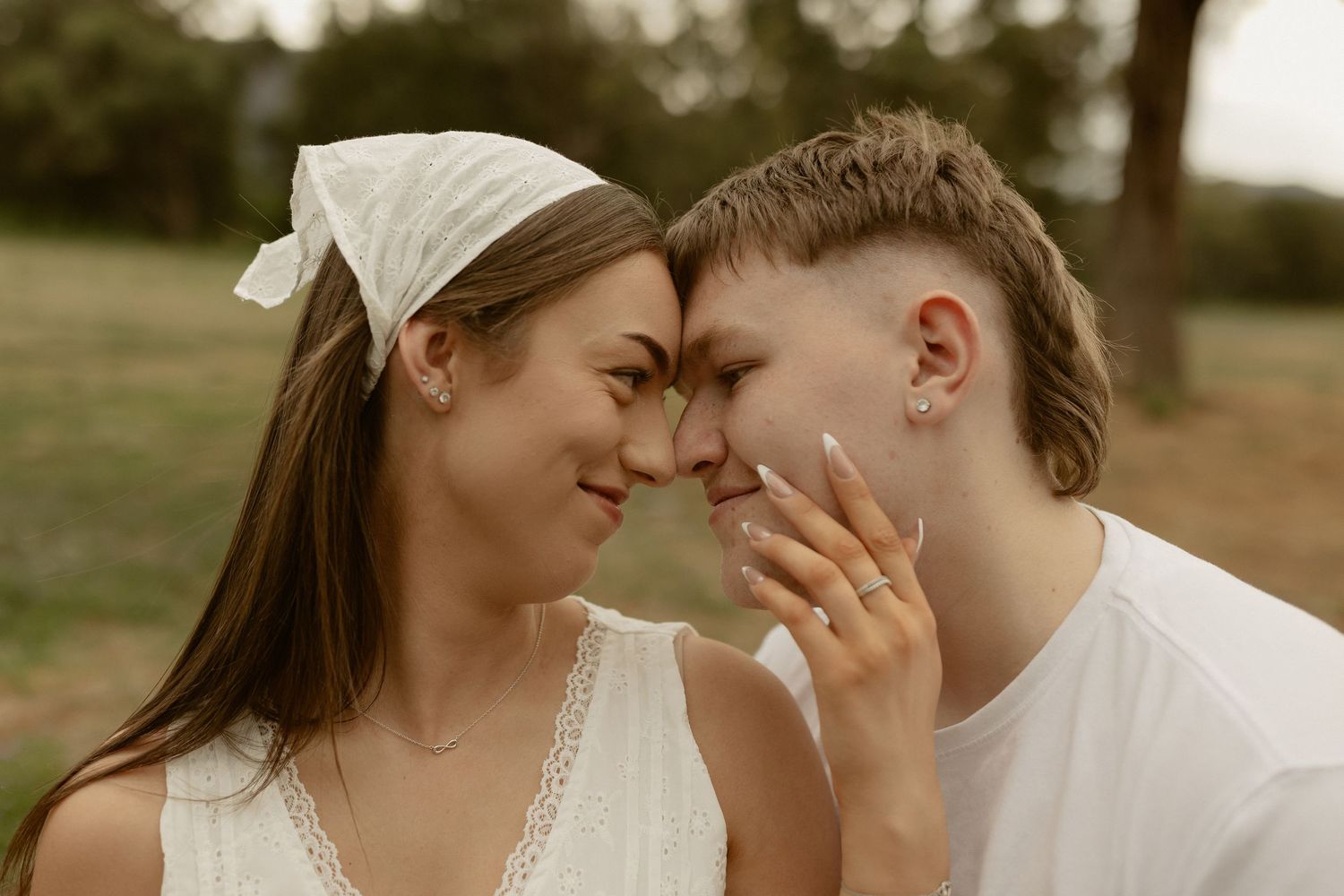 A tender romantic moment between a couple in white clothing sharing an intimate gesture outdoors.