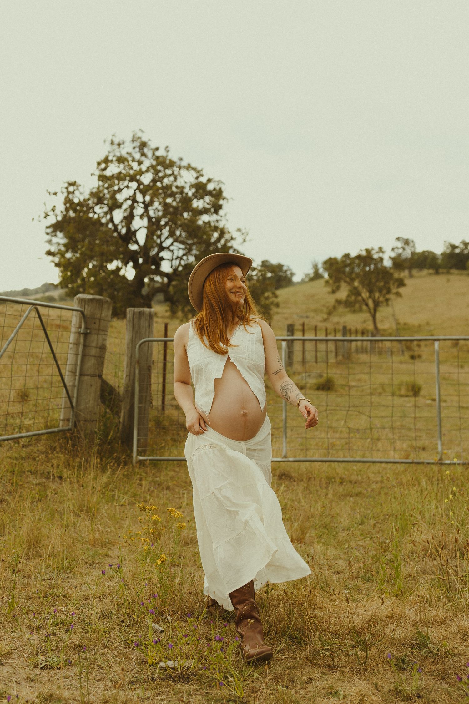 Dreamy pastoral scene with white dress and straw hat against rural farm fence and golden grass.