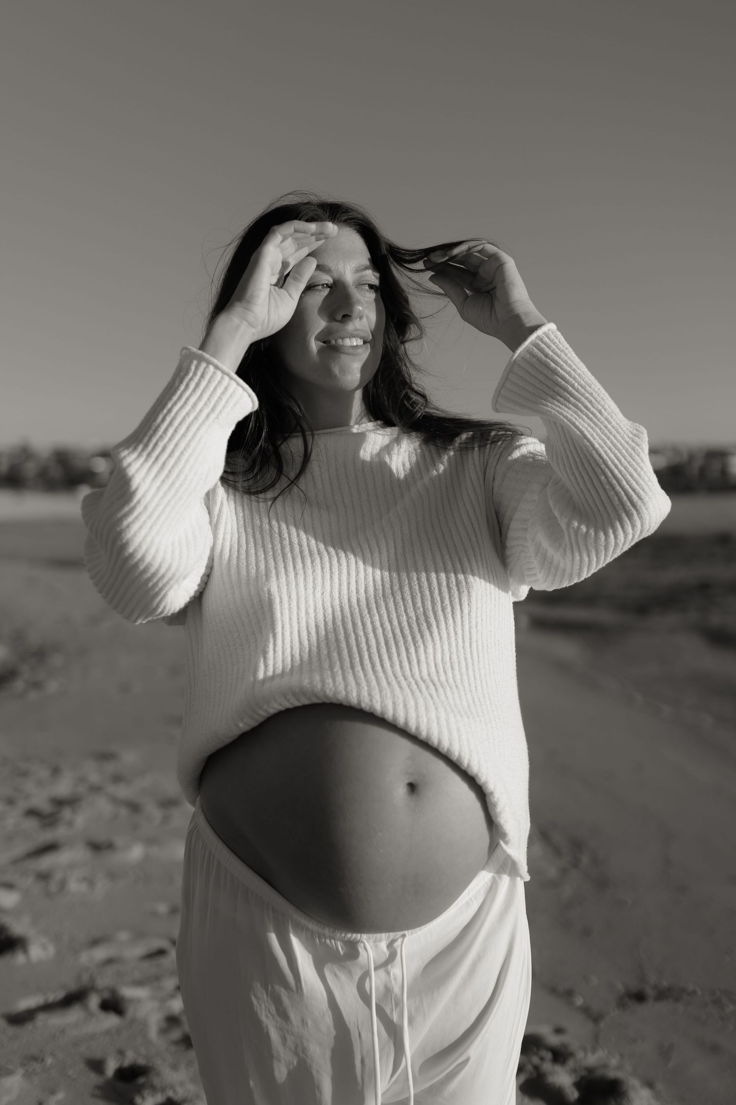 Black and white series of a pregnant woman in white sweater showing her belly.