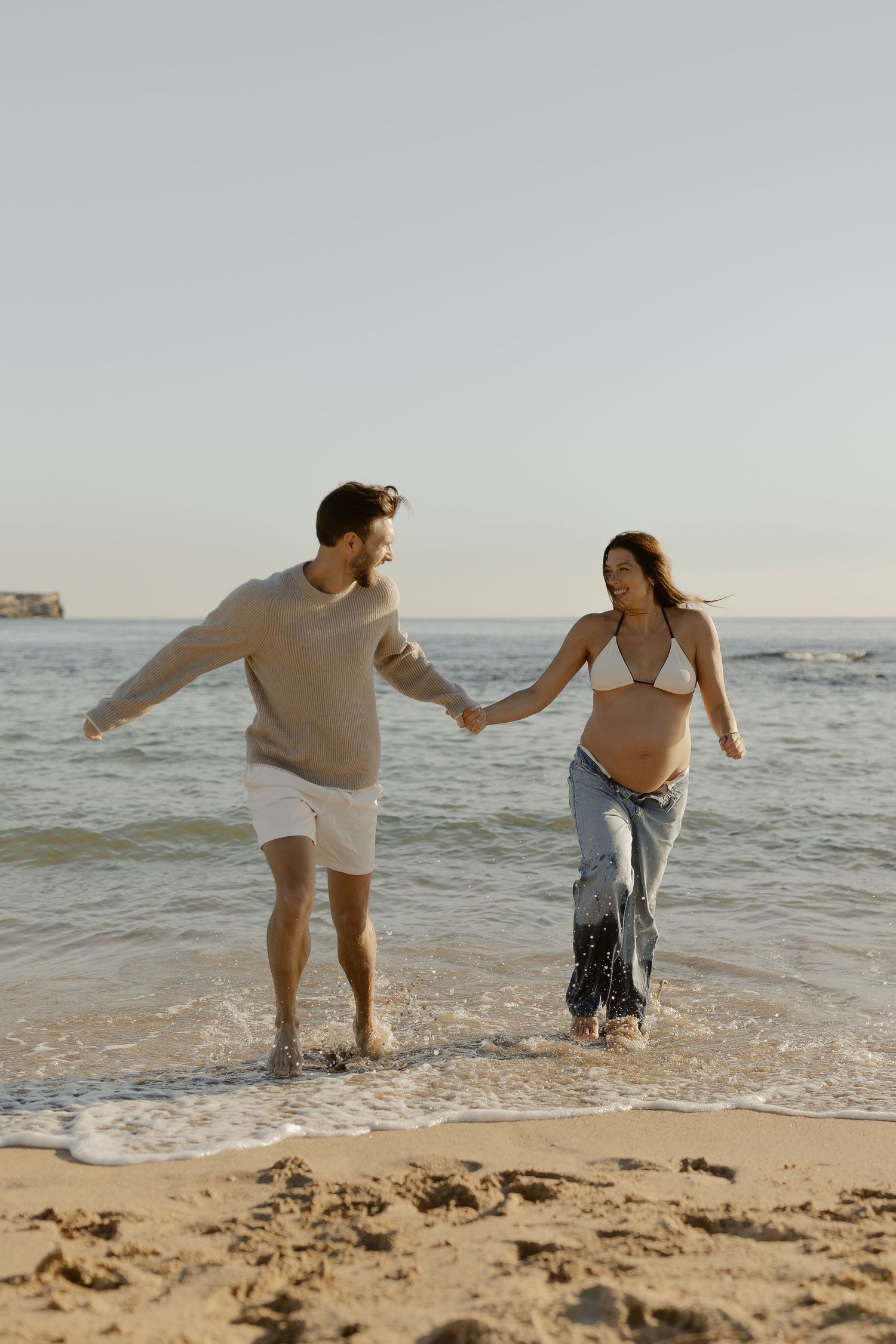 Couple splashing and playing in ocean waves at beach during sunset.