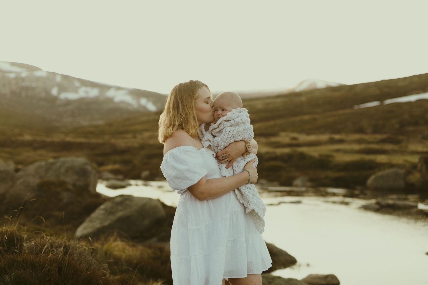 A tender moment captured at sunset by a mountain stream with snow-capped peaks in the background.