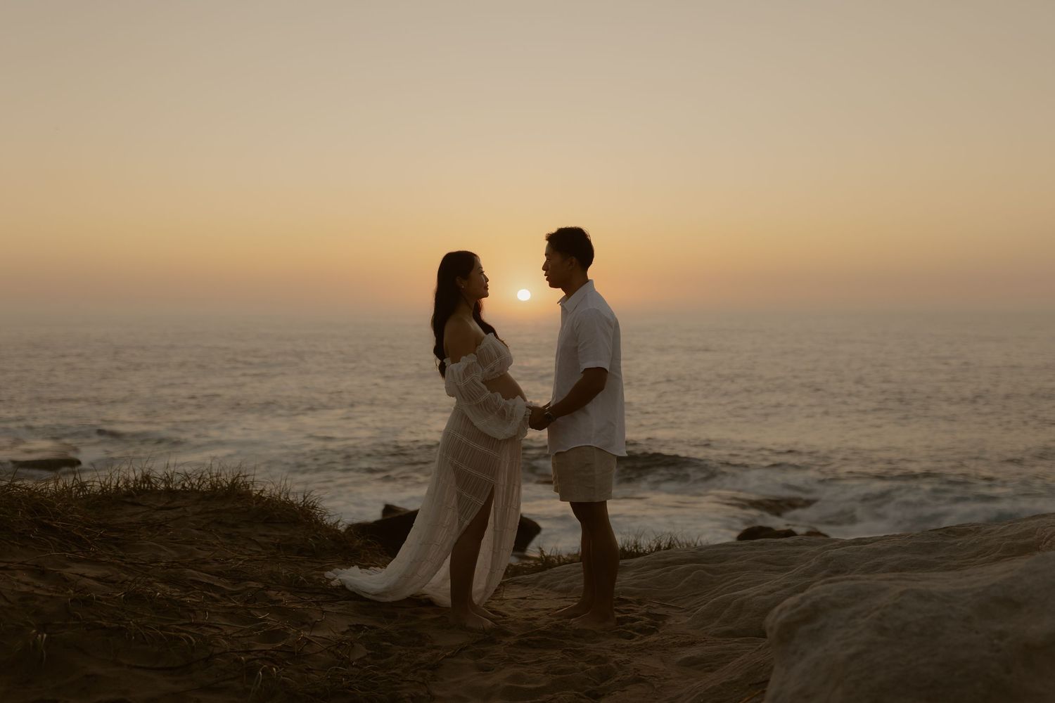 Couple sharing an intimate moment on rocky coastal cliffs during golden hour sunset.