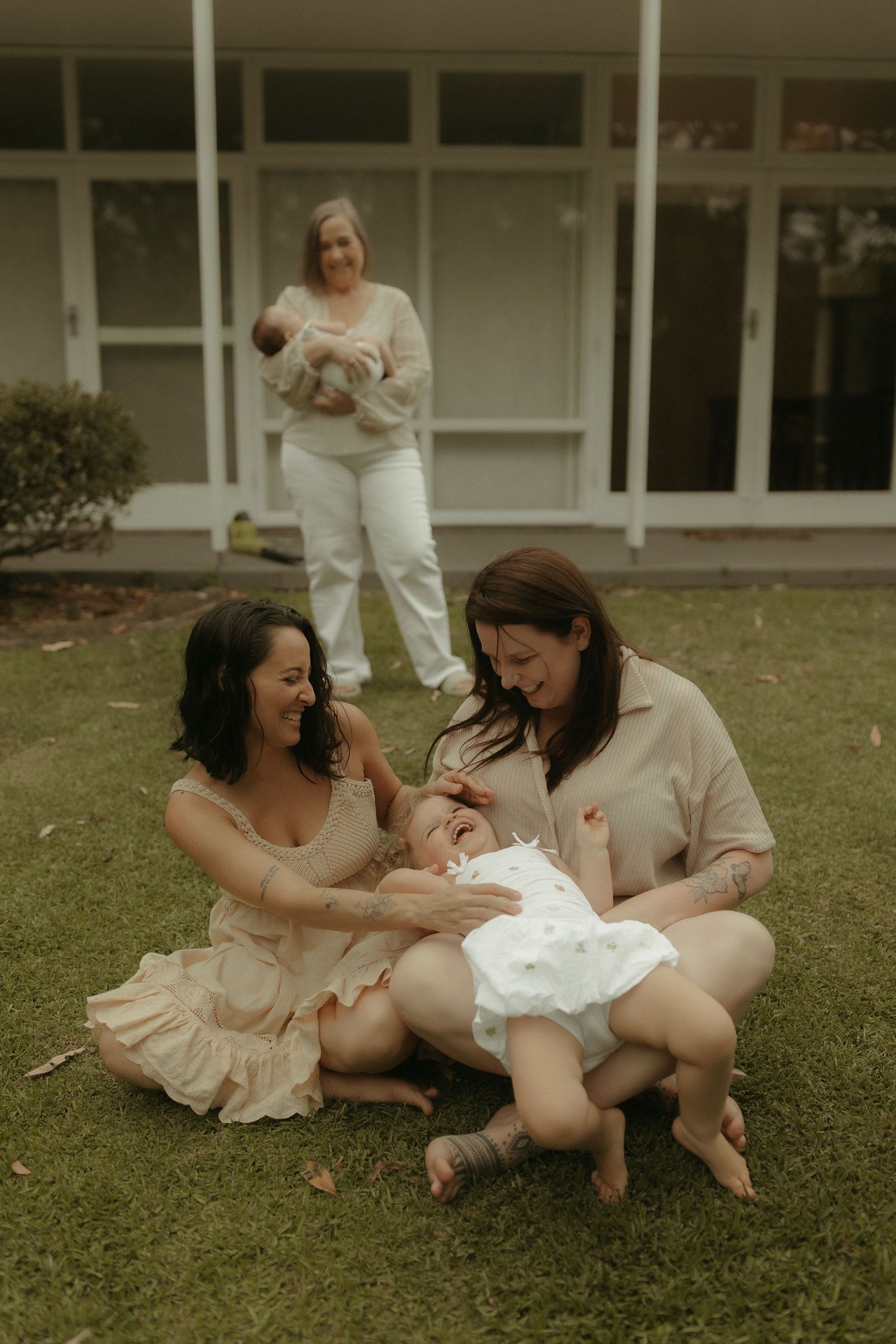 A joyful outdoor family photoshoot on grass with people wearing light colored clothing.