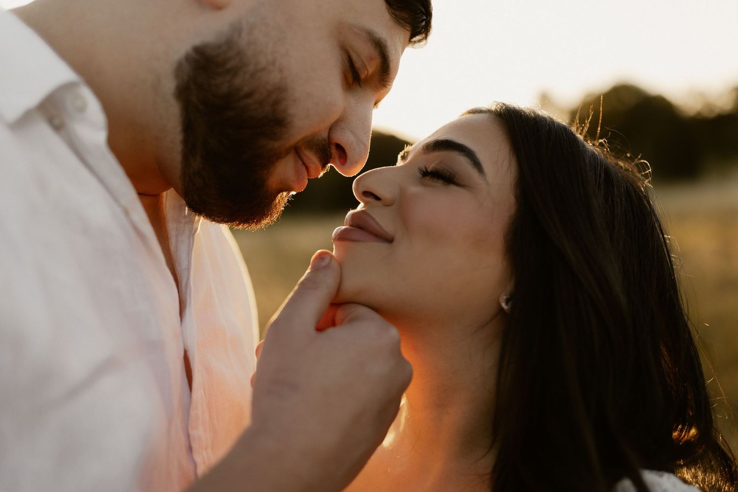 Intimate couple shares tender moments in a glowing field at golden hour.