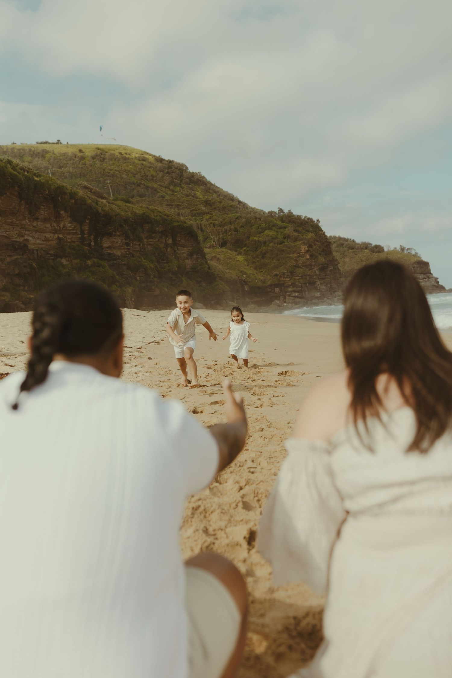 People in white clothing walking and playing along a scenic rocky beach under cloudy skies.