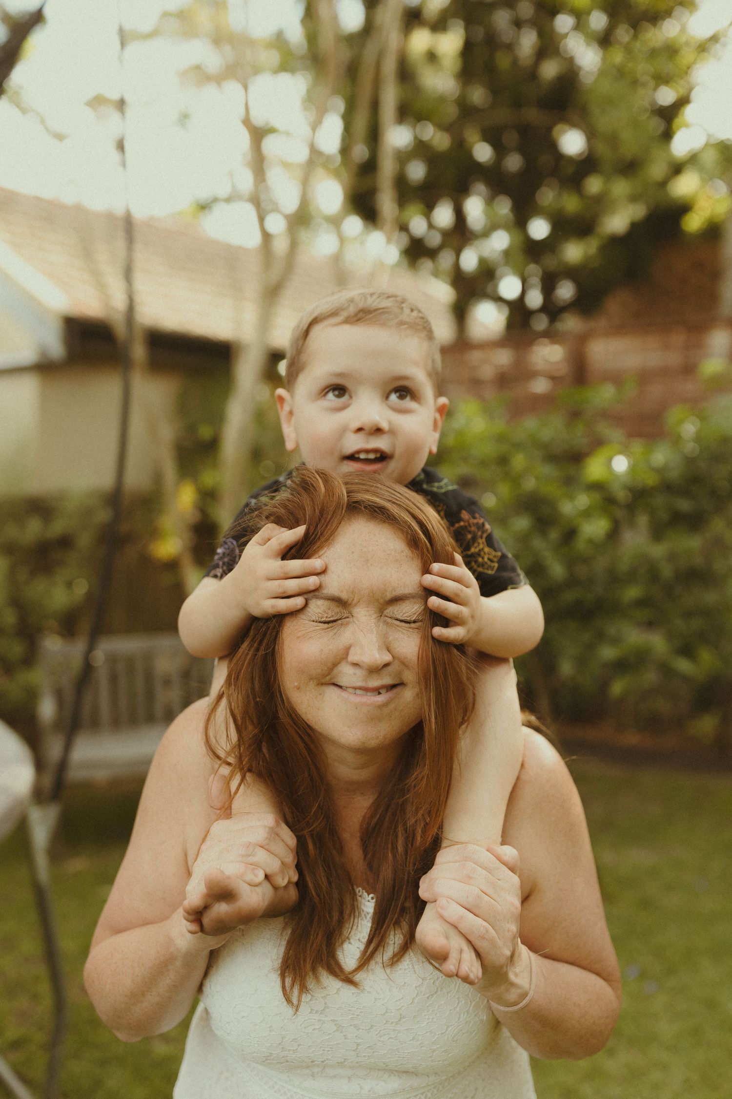A playful moment captured in a backyard with joyful expressions and raised hands in warm sunlight.