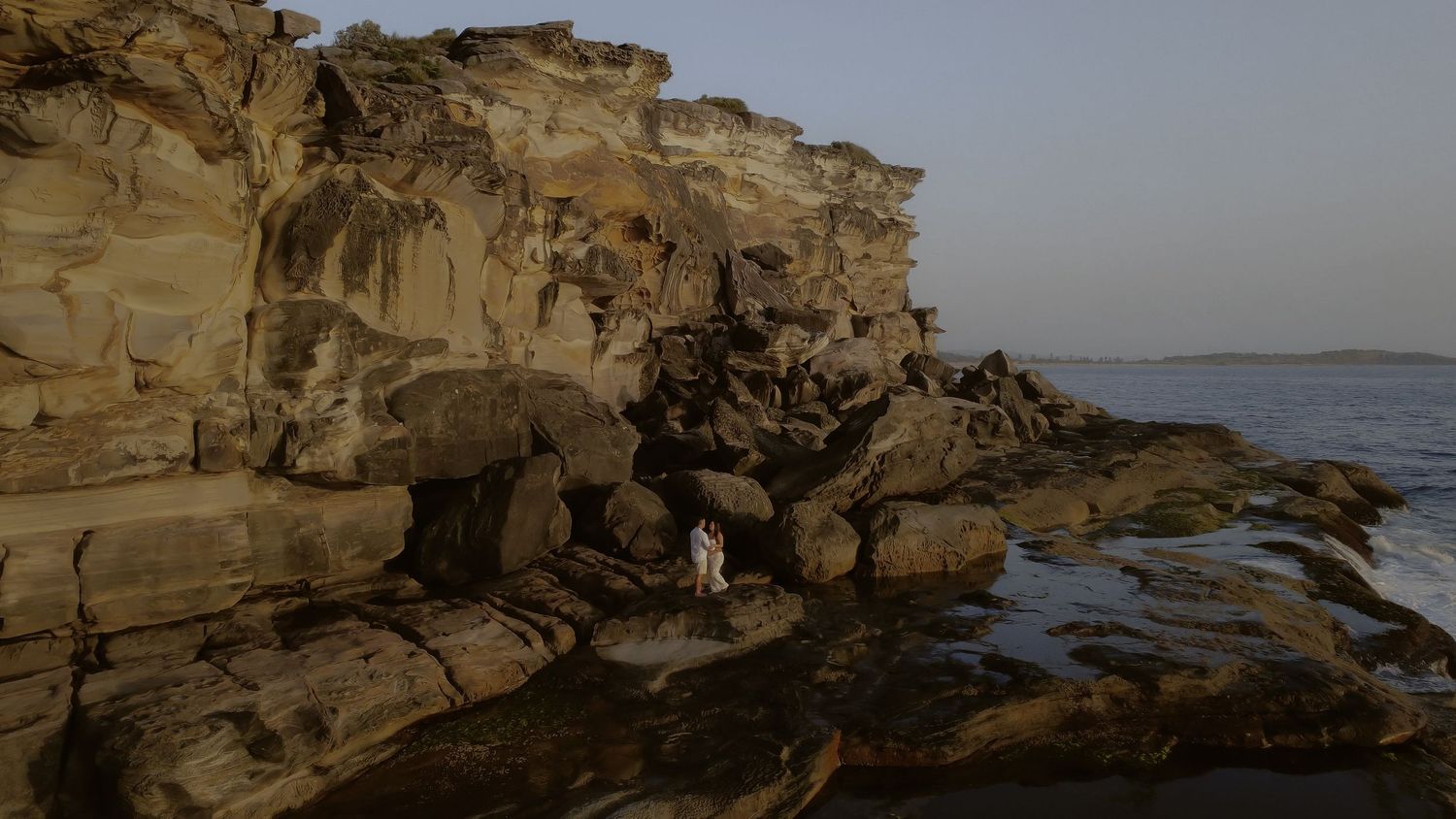 Panoramic view of rugged coastal cliffs with layered sandstone formations along a rocky shoreline at sunset.