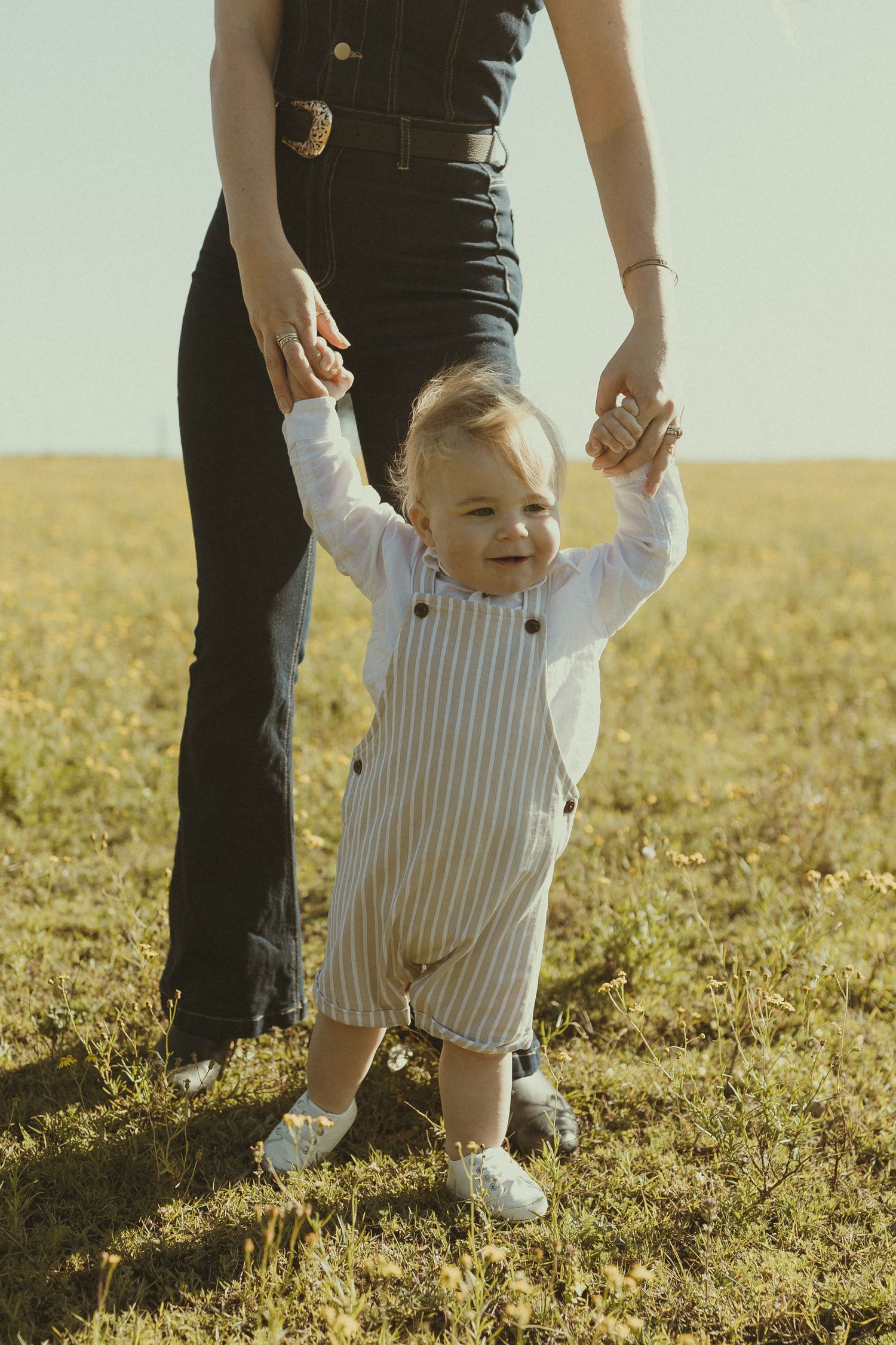 A series of photos showing a small child learning to walk in a sunny field while wearing striped overalls.