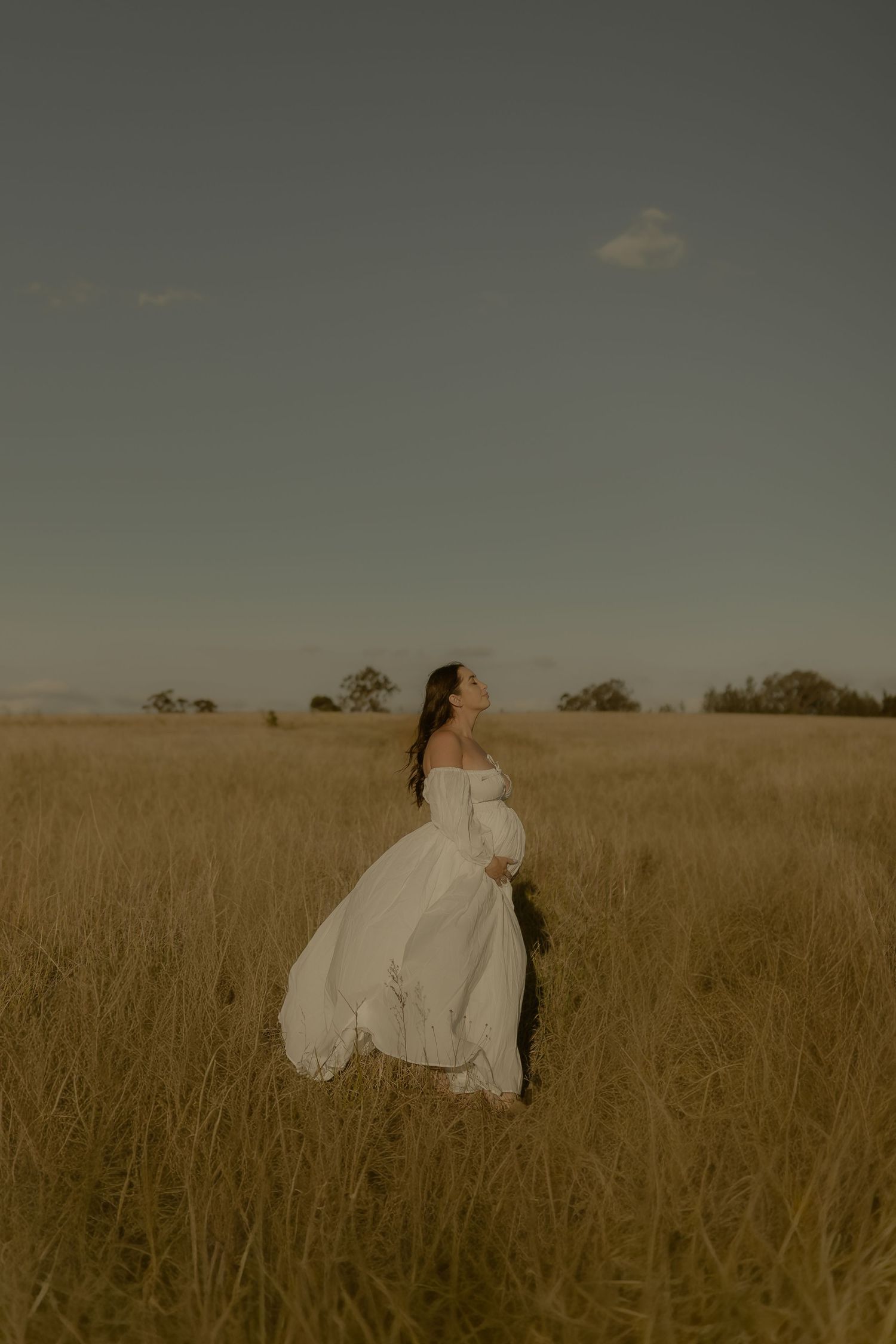 A romantic couple in wedding attire embraces in a golden wheat field at sunset.