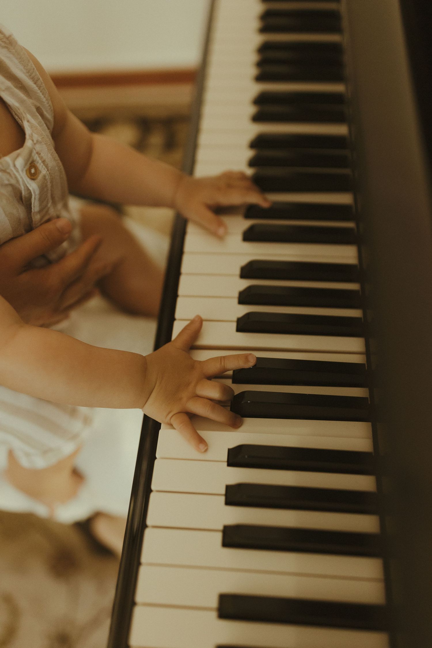 Small hands reach out to play piano keys in a warm-toned indoor setting.