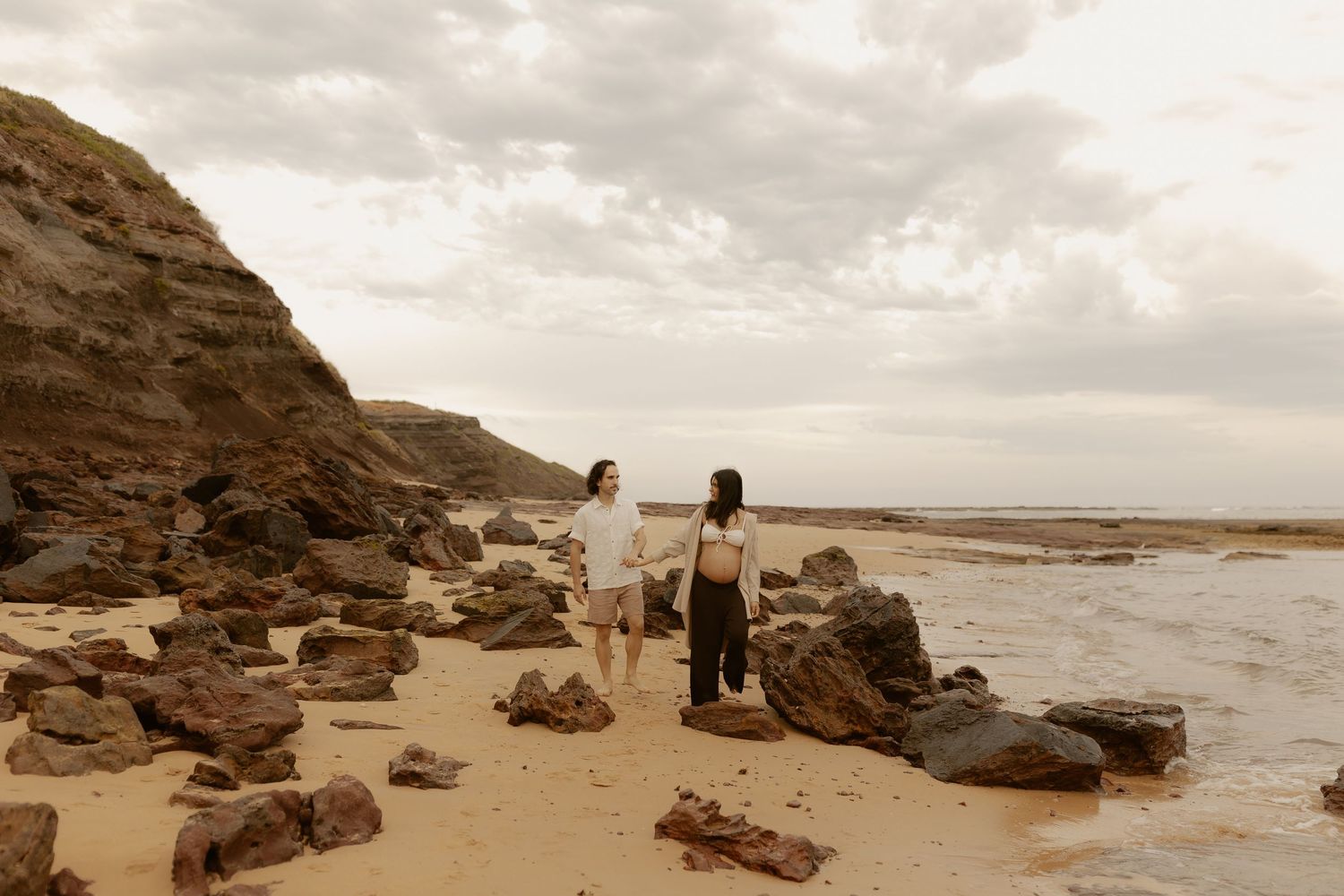 A sepia-toned photo of a couple walking along a rocky beach coastline.