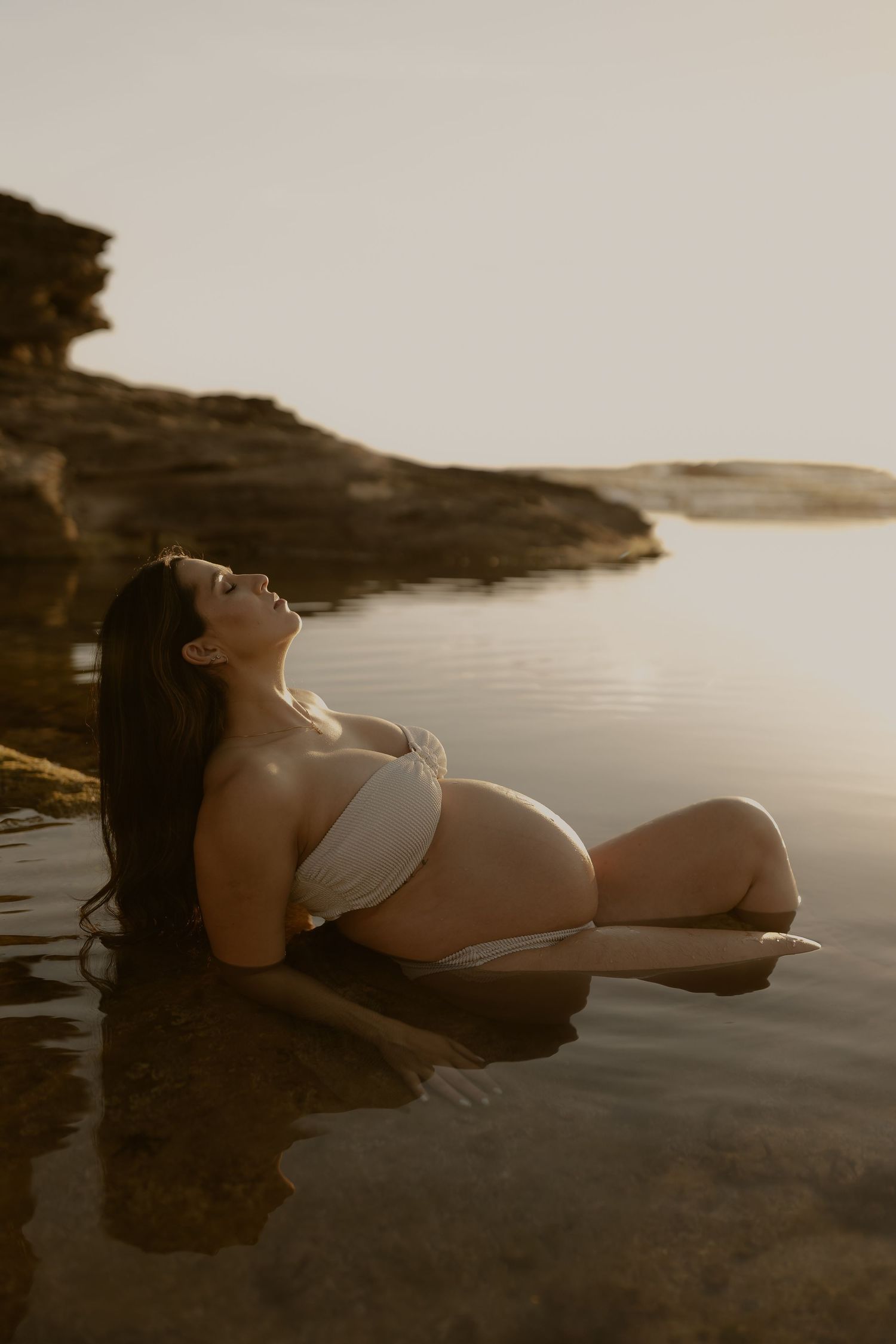 A person in white swimwear lounges by a serene lake at sunset, creating a peaceful silhouette against the water.