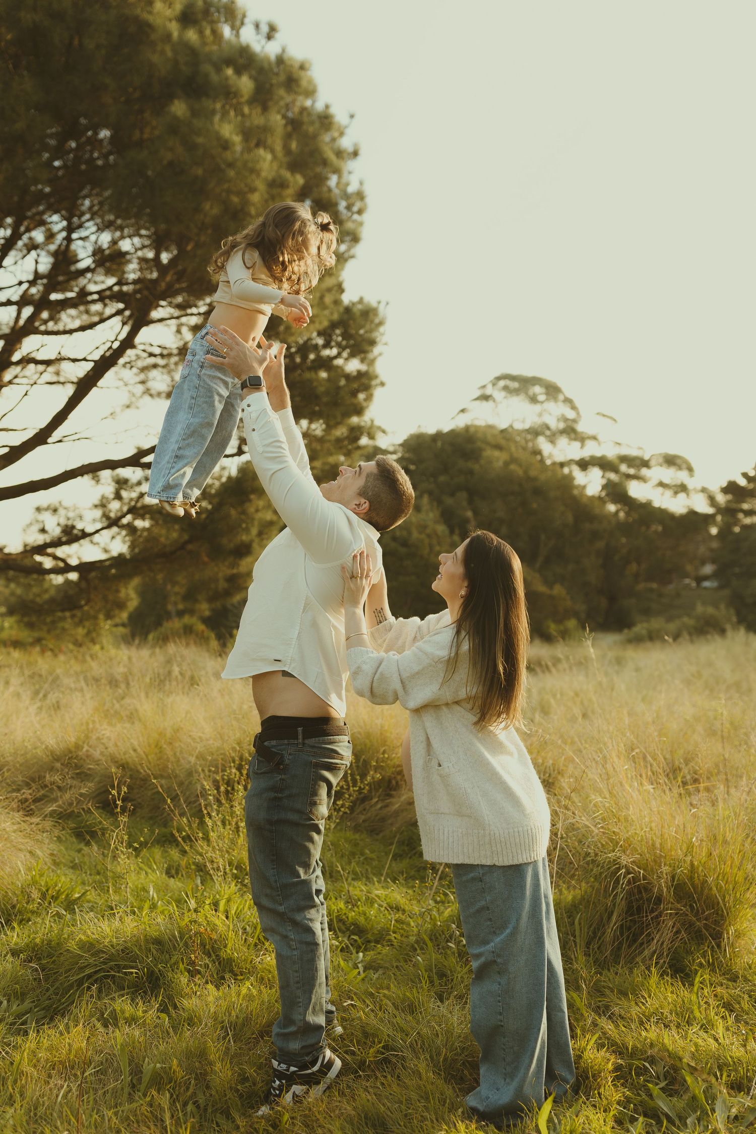 A romantic couple dances playfully together in a sunlit field during golden hour.