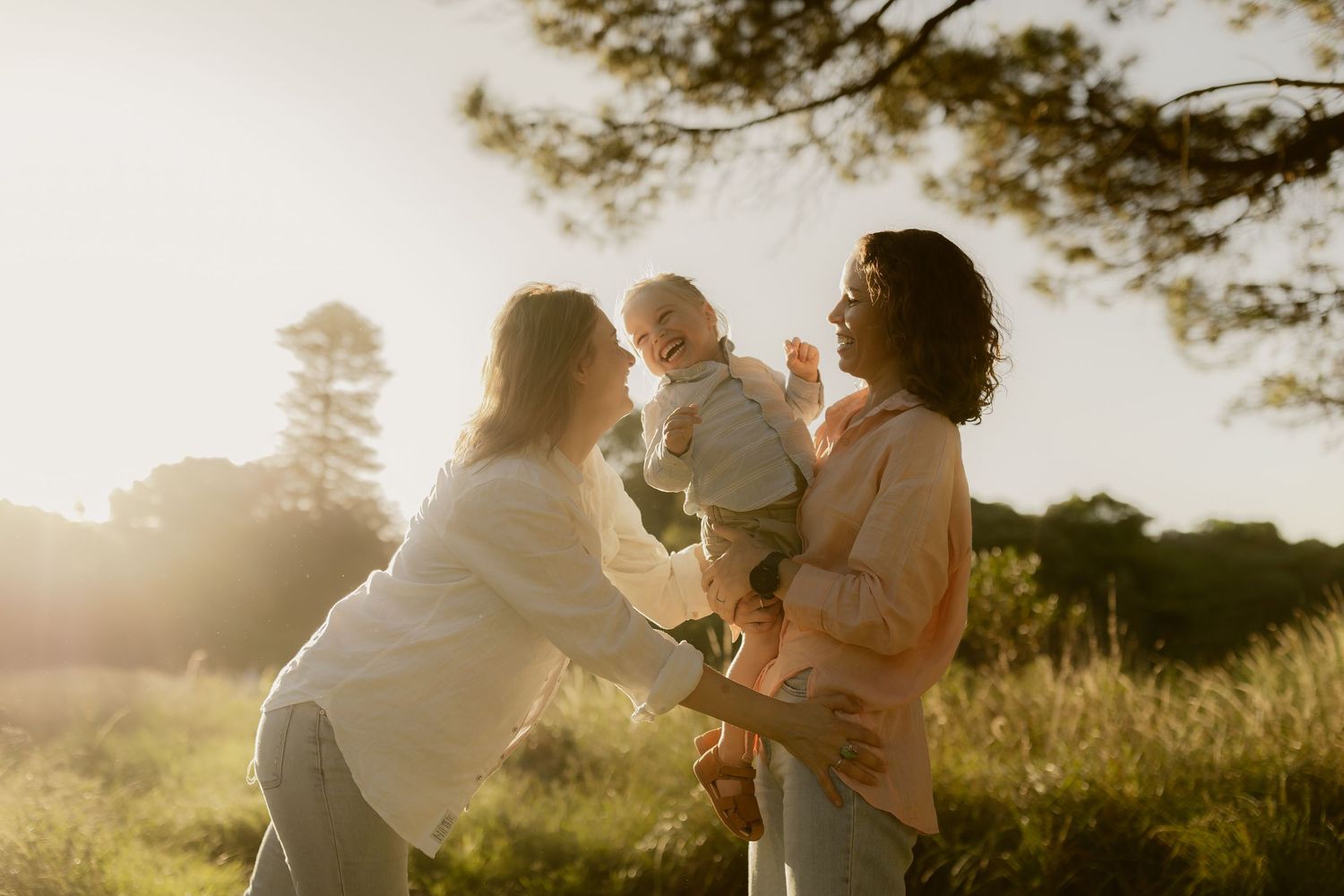 Family embracing in a sunlit field with trees silhouetted against the sky.