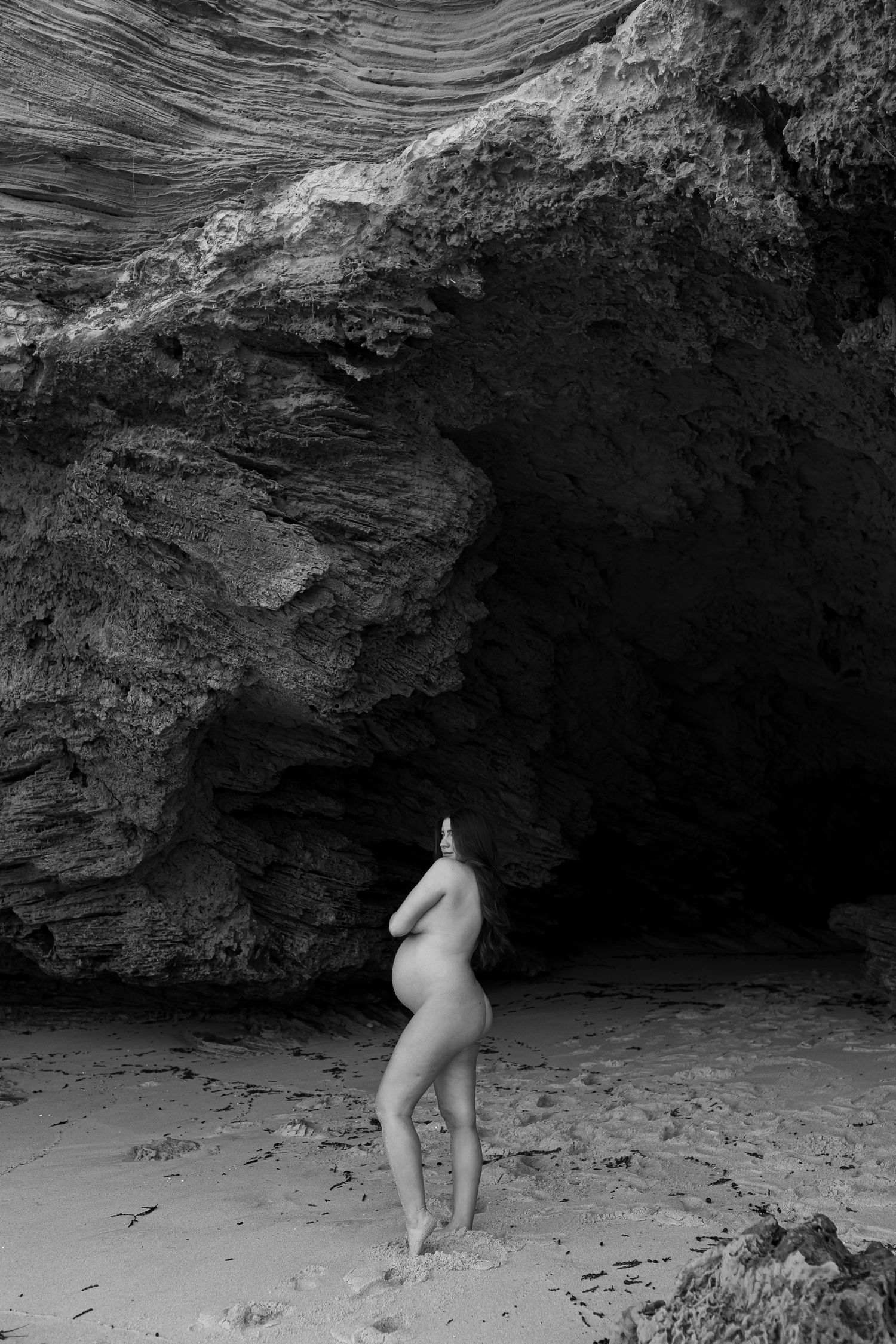 Black and white artistic photo of figure silhouetted against dramatic coastal cave entrance and rock formations.