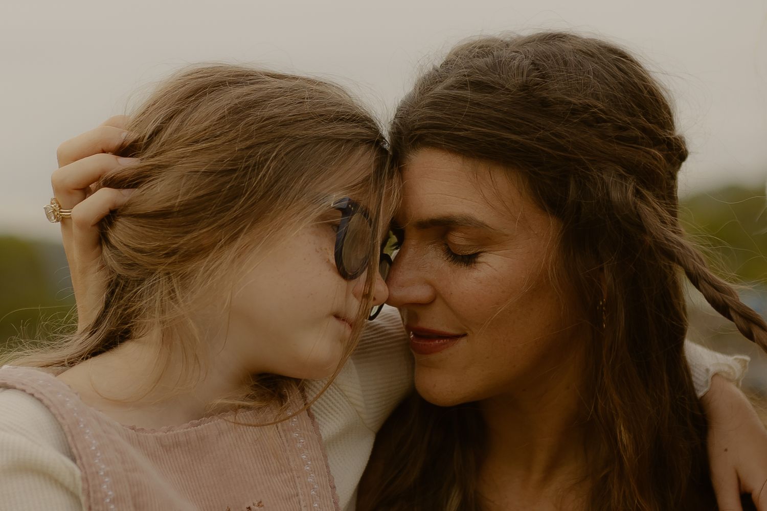 Mother and daughter touching foreheads in tender close-up outdoor portrait.