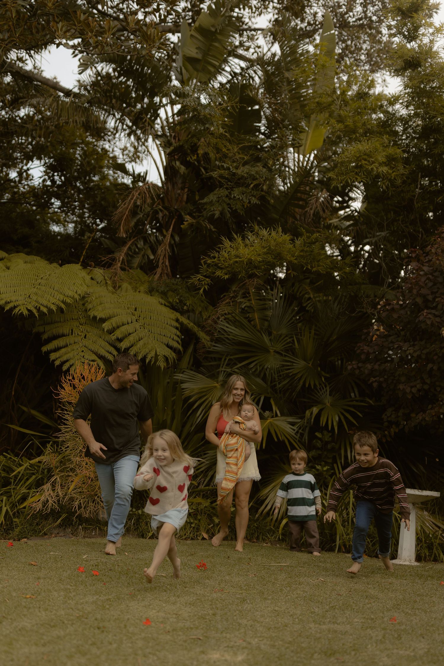 A joyful family with young children running and playing together in a lush green garden outdoors.