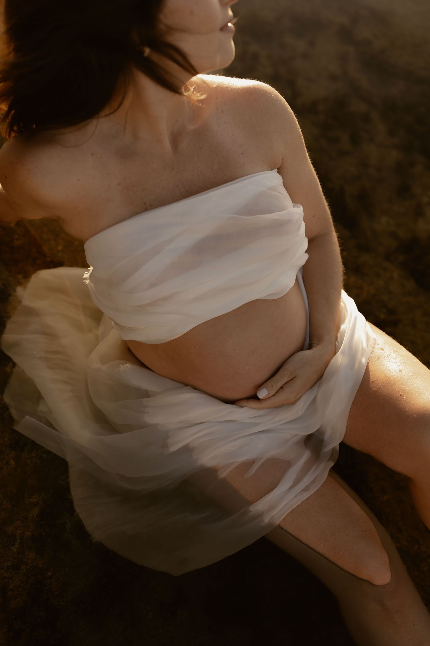 Ethereal white fabric drapes elegantly across a person's body in dramatic golden sunlight creating soft flowing forms.