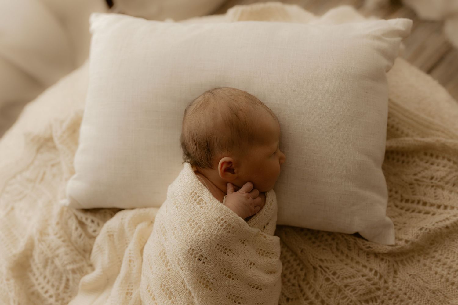 A newborn baby wrapped in white blankets sleeps peacefully in a hospital bassinet.