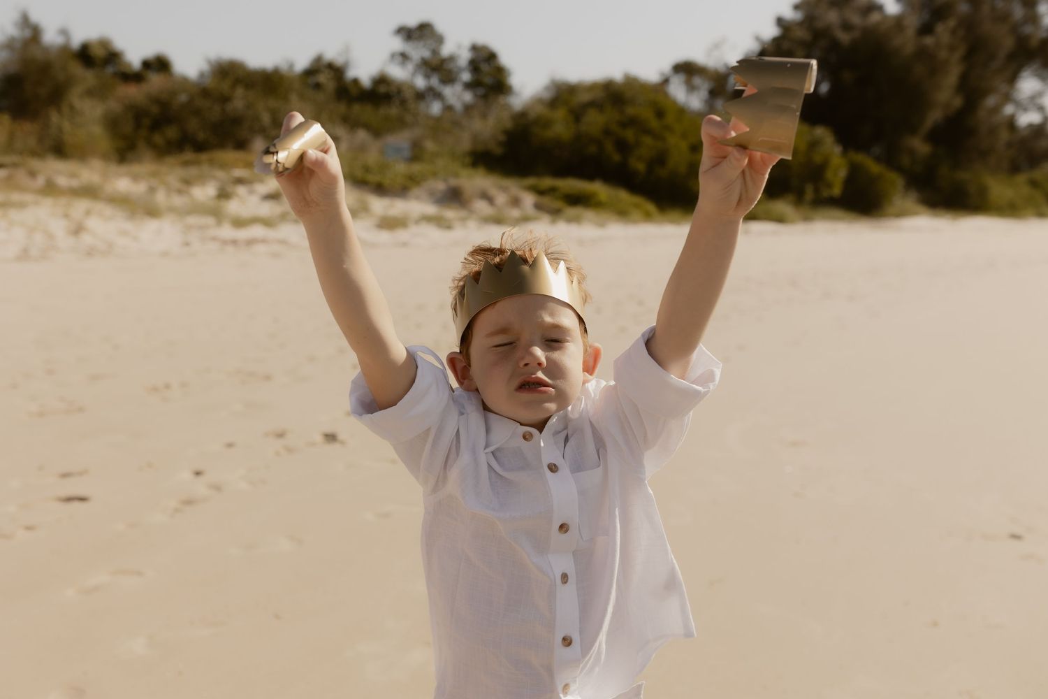 Person raising arms triumphantly against bright beach background.