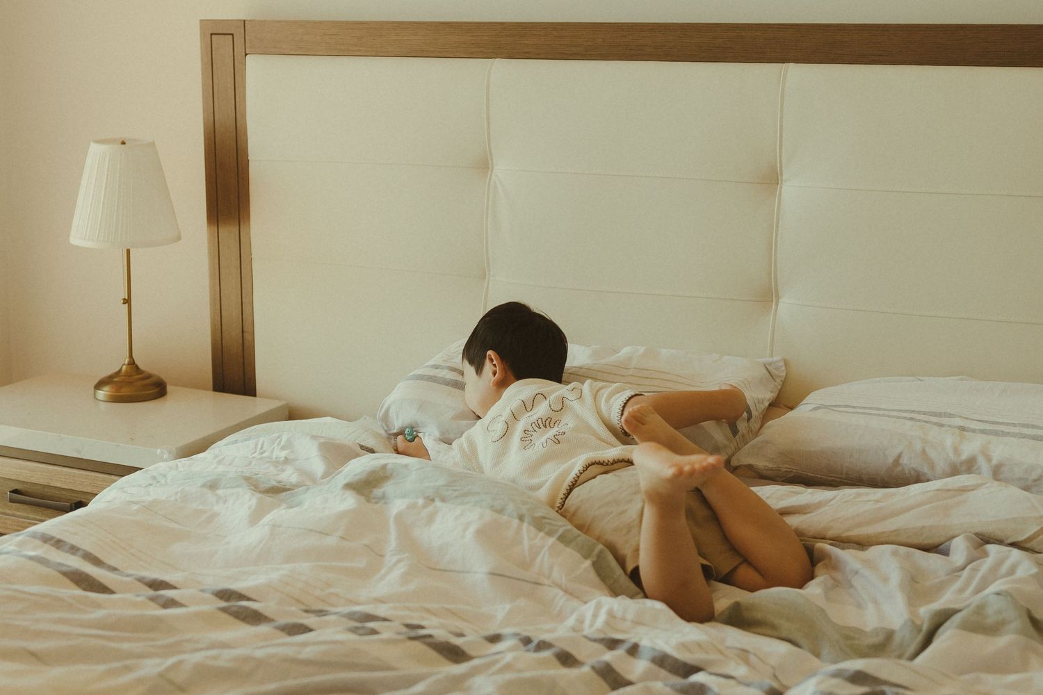 Someone sleeping peacefully in a white bed with rumpled sheets and a bedside lamp in a bright, minimalist bedroom.