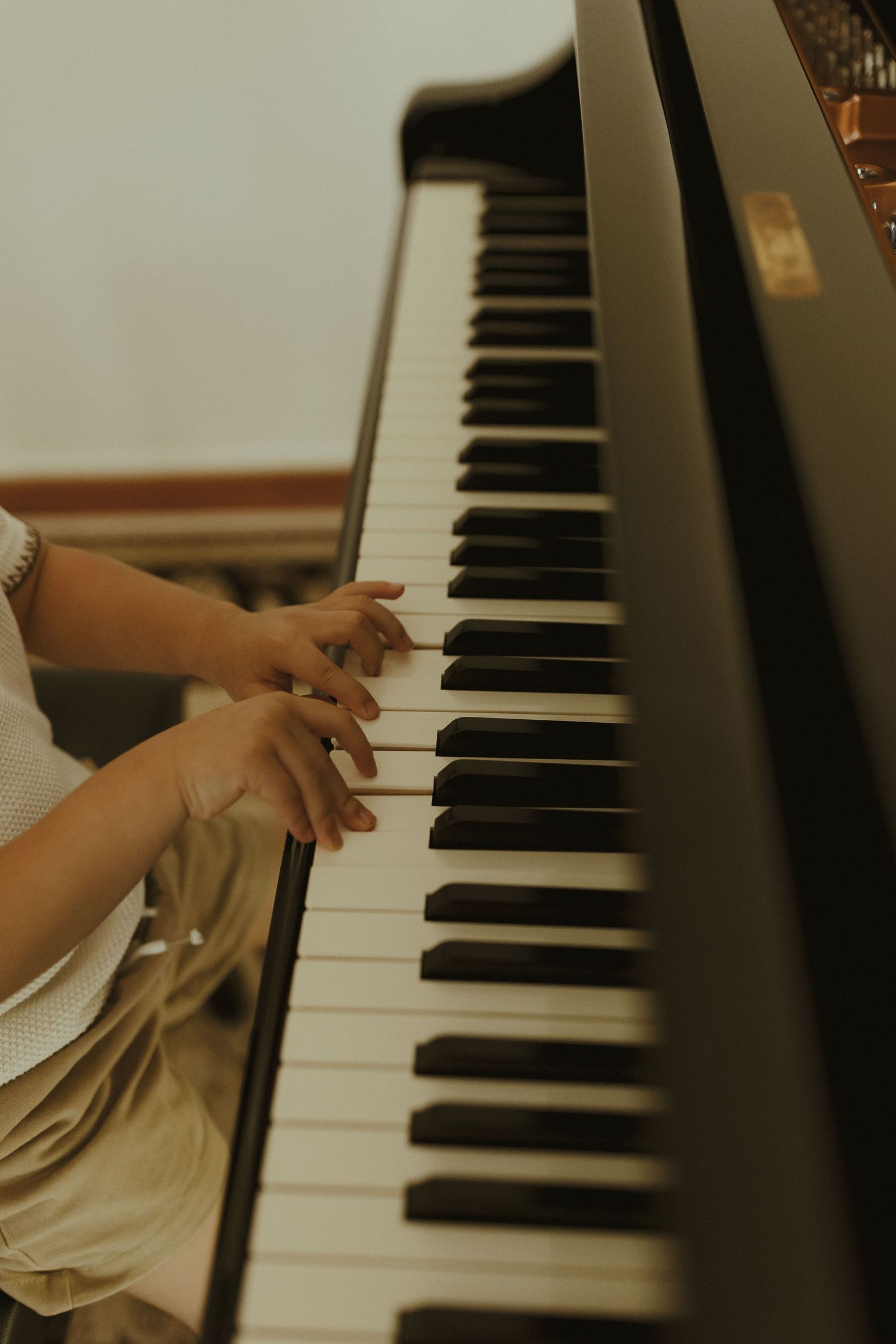 Hands playing on black and white piano keys in warm lighting.