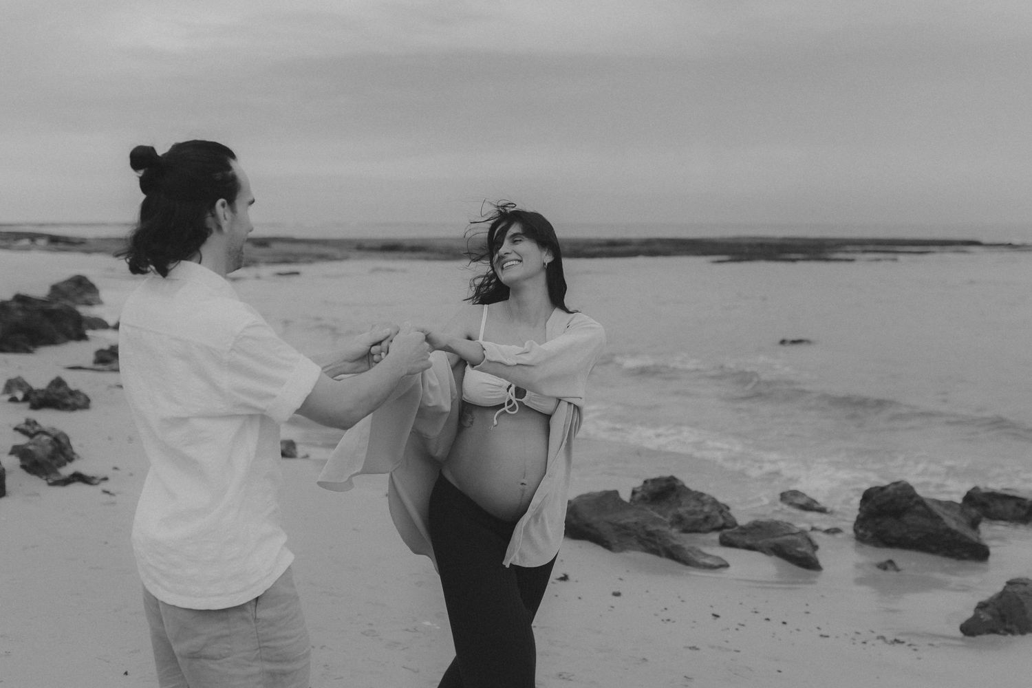 Couple enjoys playful moment together on windswept beach.