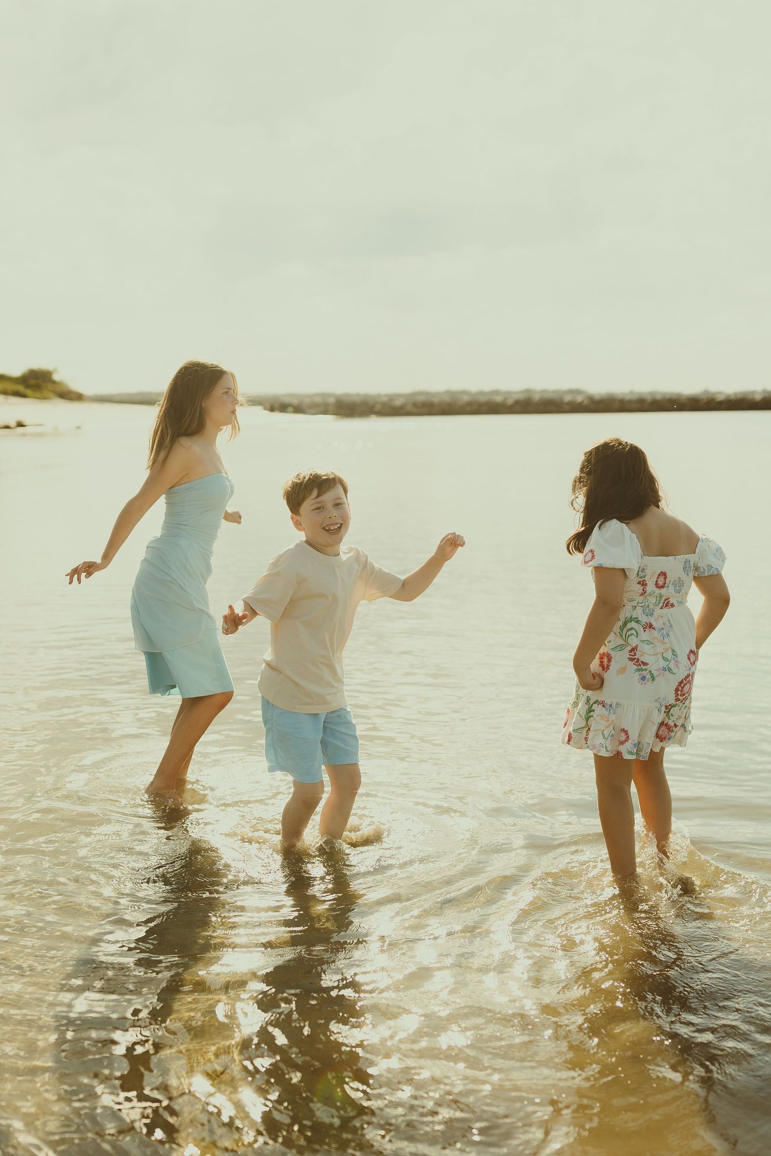 Three people splashing and playing in shallow ocean water during golden hour at the beach.