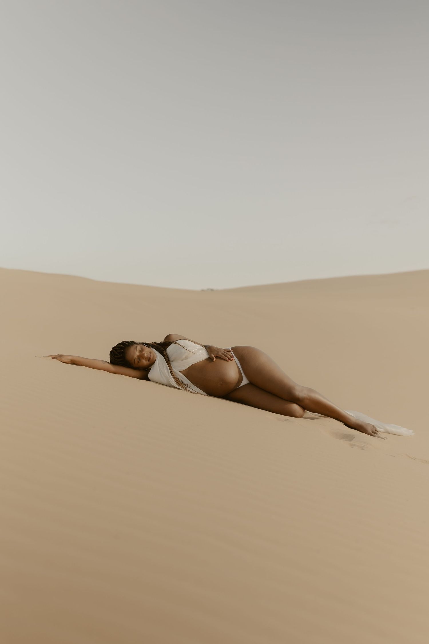 Figure lying on smooth desert sand dunes in minimalist artistic composition.
