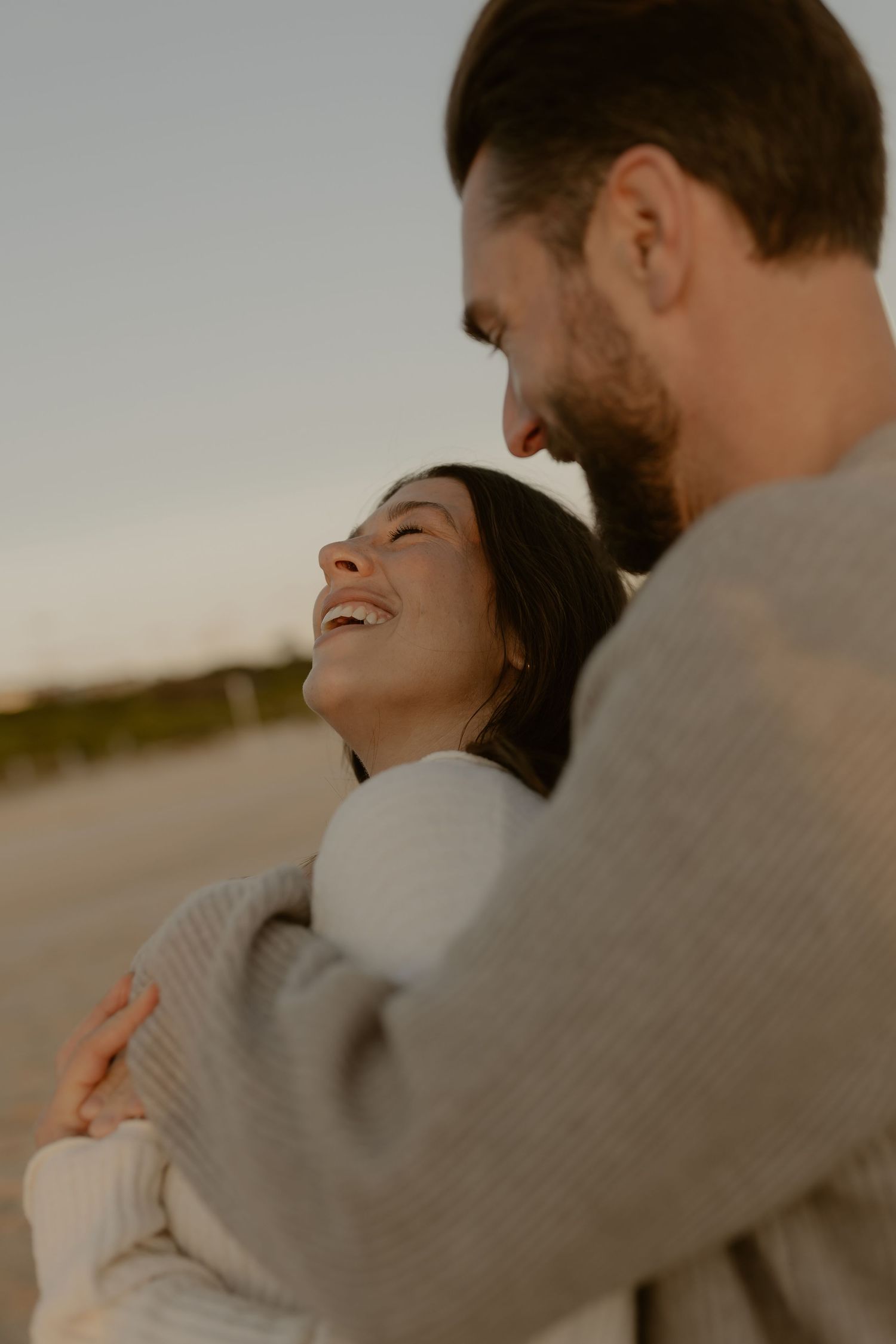 An intimate moment between a couple laughing together during a sunset beach photoshoot.