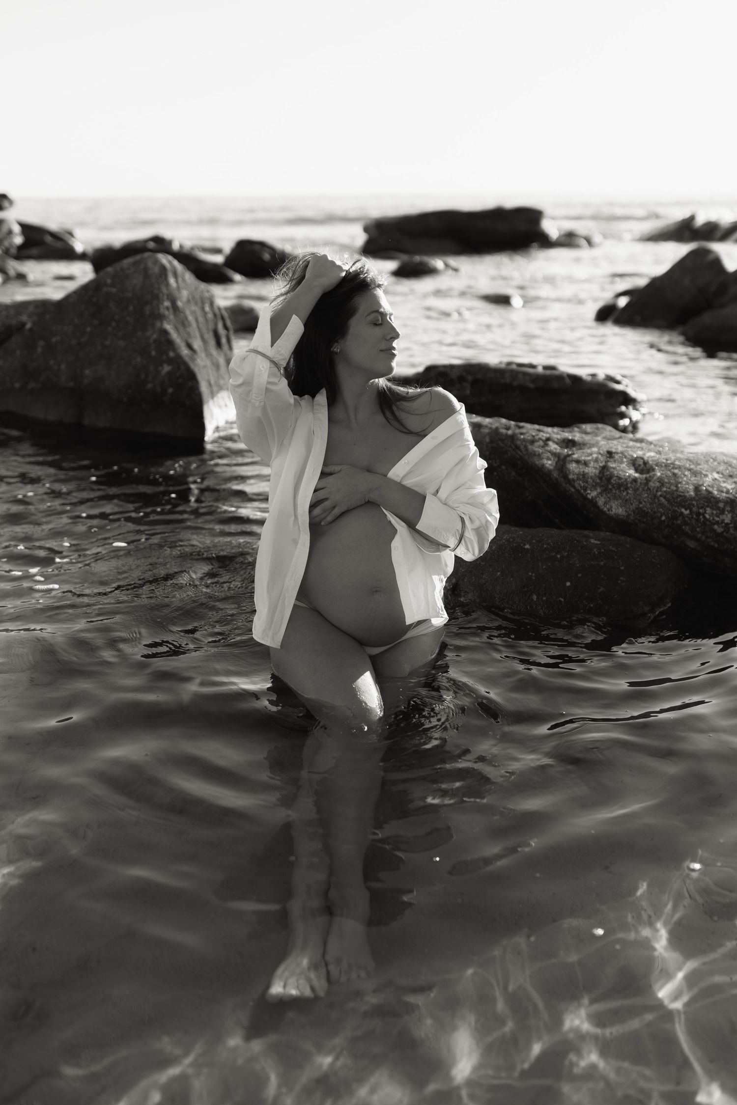 A black and white beach photoshoot with waves crashing against rocks.