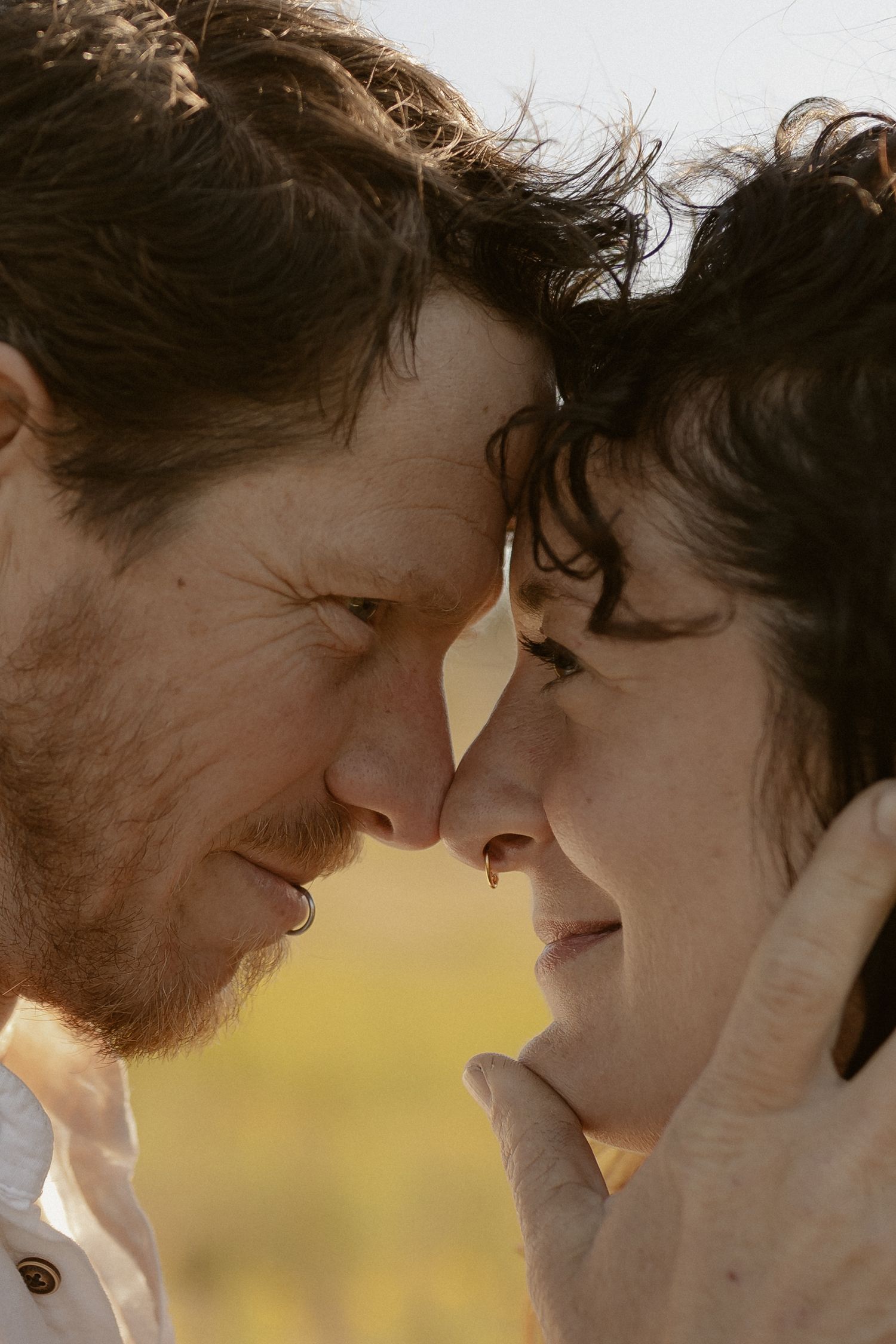 An intimate close-up moment between a couple touching foreheads in warm sunlight.