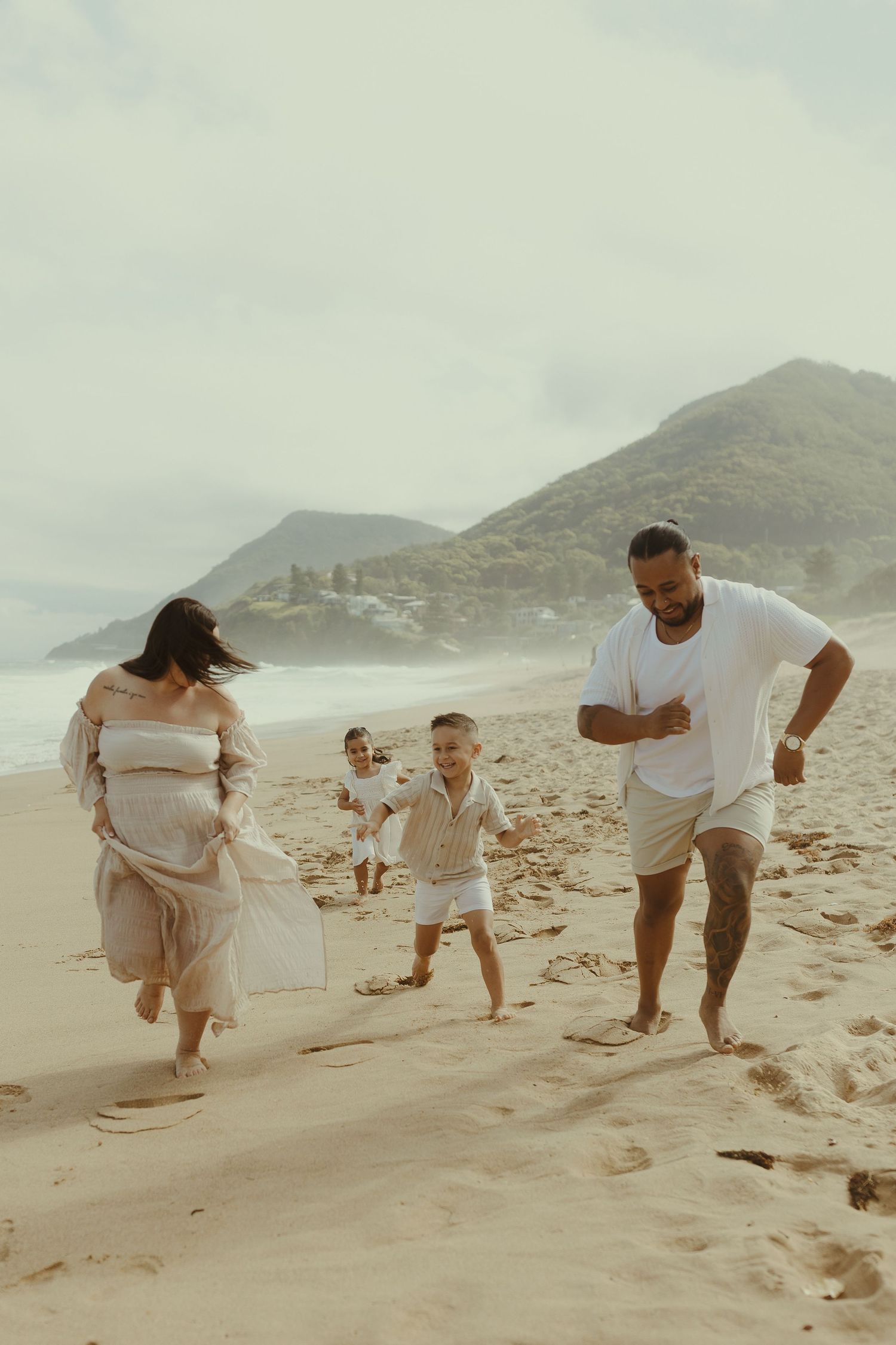 Family plays together on a sandy beach with mountains in the background on a cloudy day.