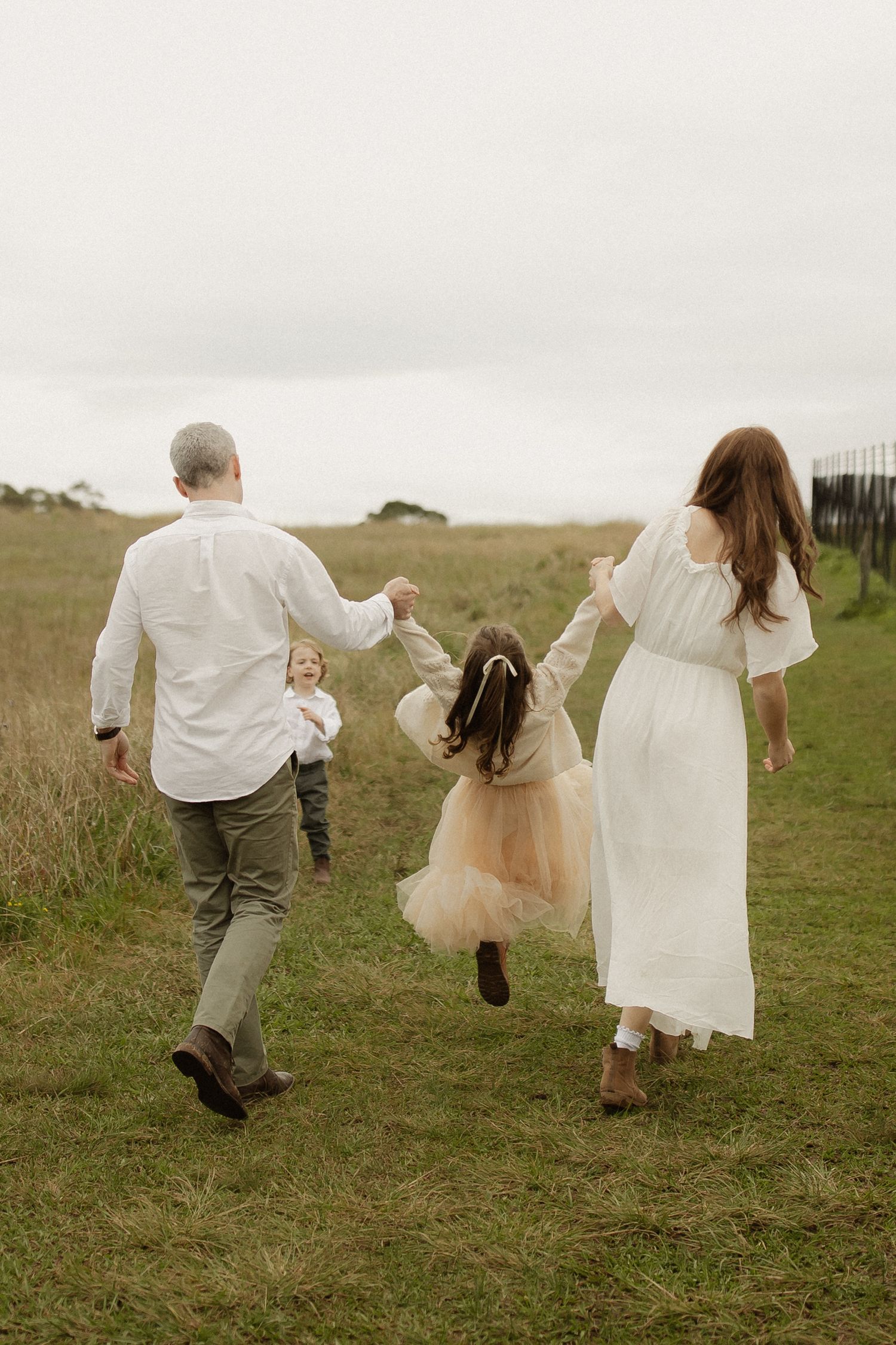 A group in white clothing runs through a grassy meadow on an overcast day.