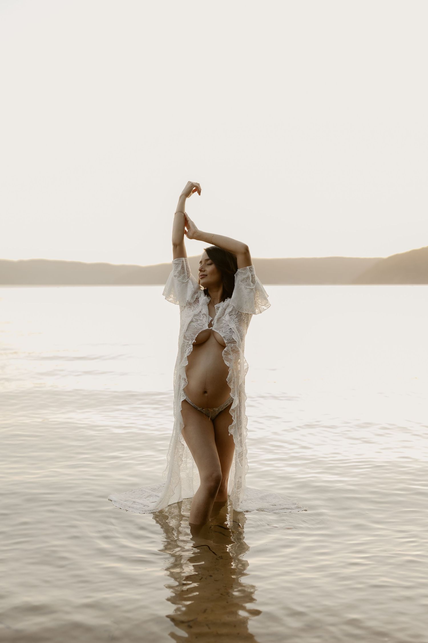 A maternity photoshoot in shallow waters at sunset with flowing white fabric.