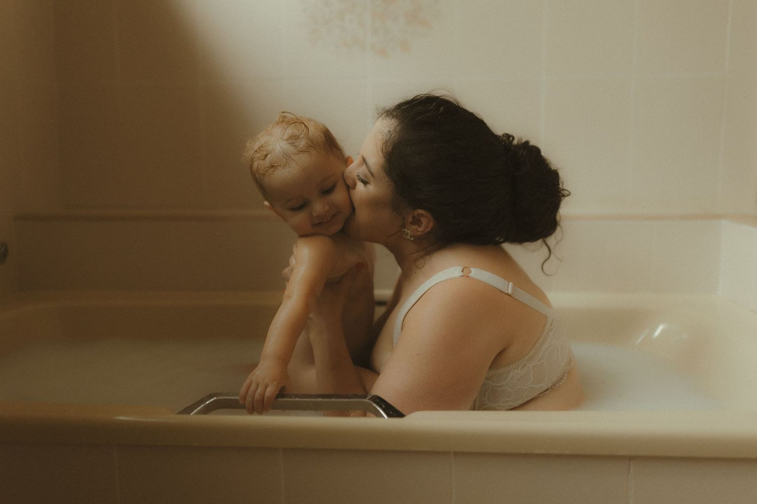 A tender moment shared between two people in a bathtub with soft, warm lighting creating an intimate atmosphere.