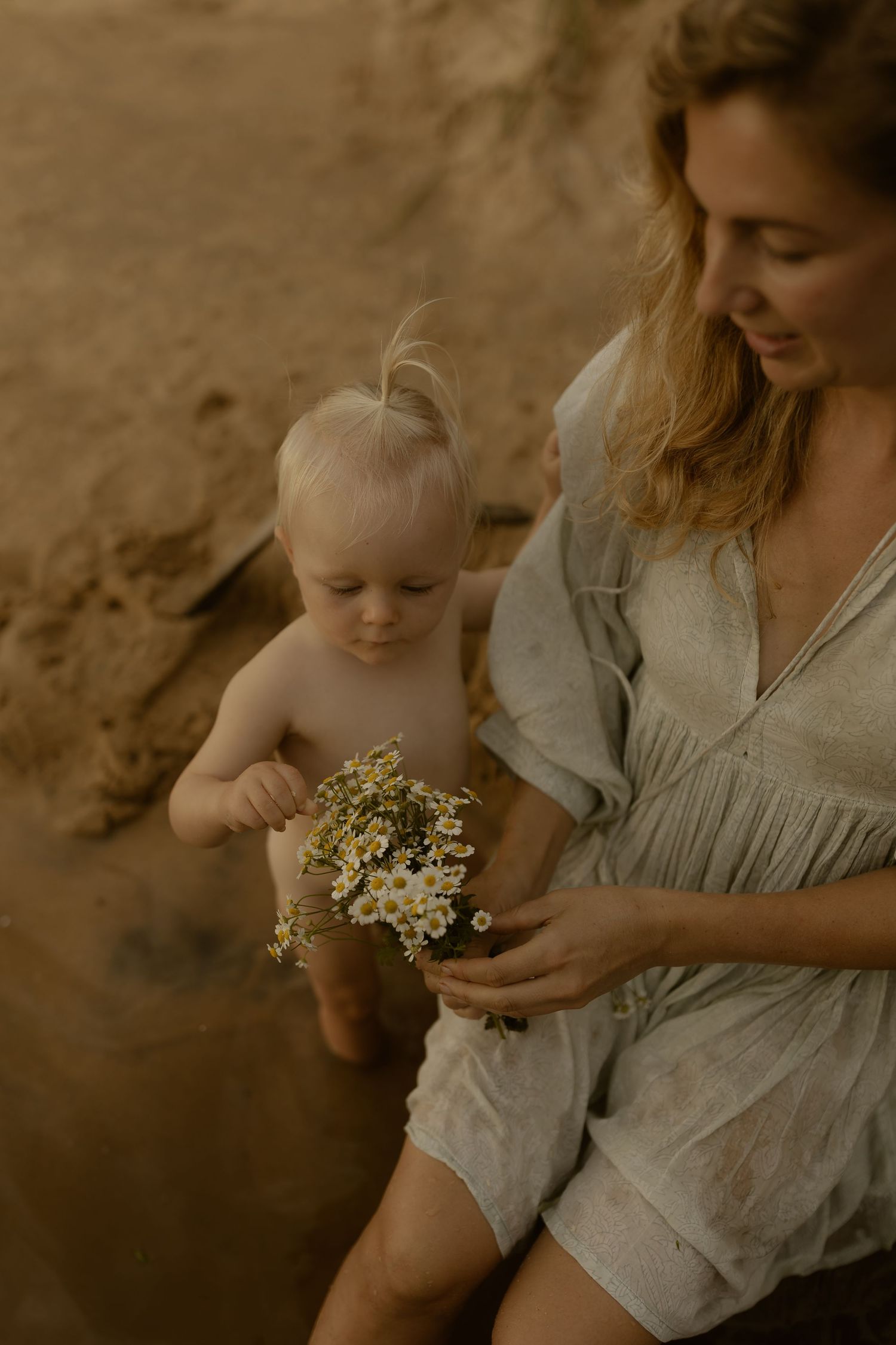 A tender moment examining wildflowers together against a rocky coastal backdrop.