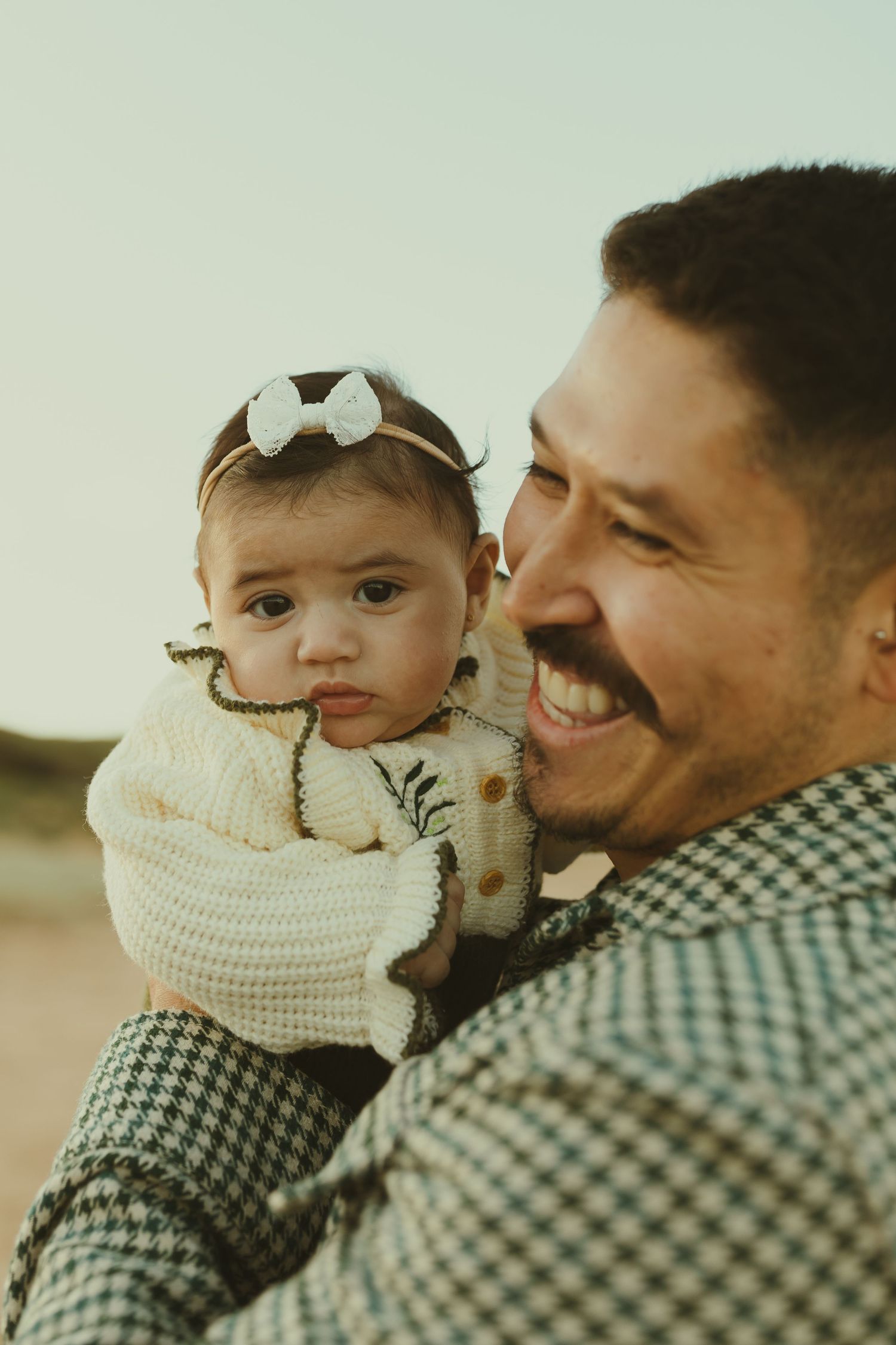 A heartwarming series of images showing a parent bonding with a baby wearing a cozy cream sweater outdoors at sunset.