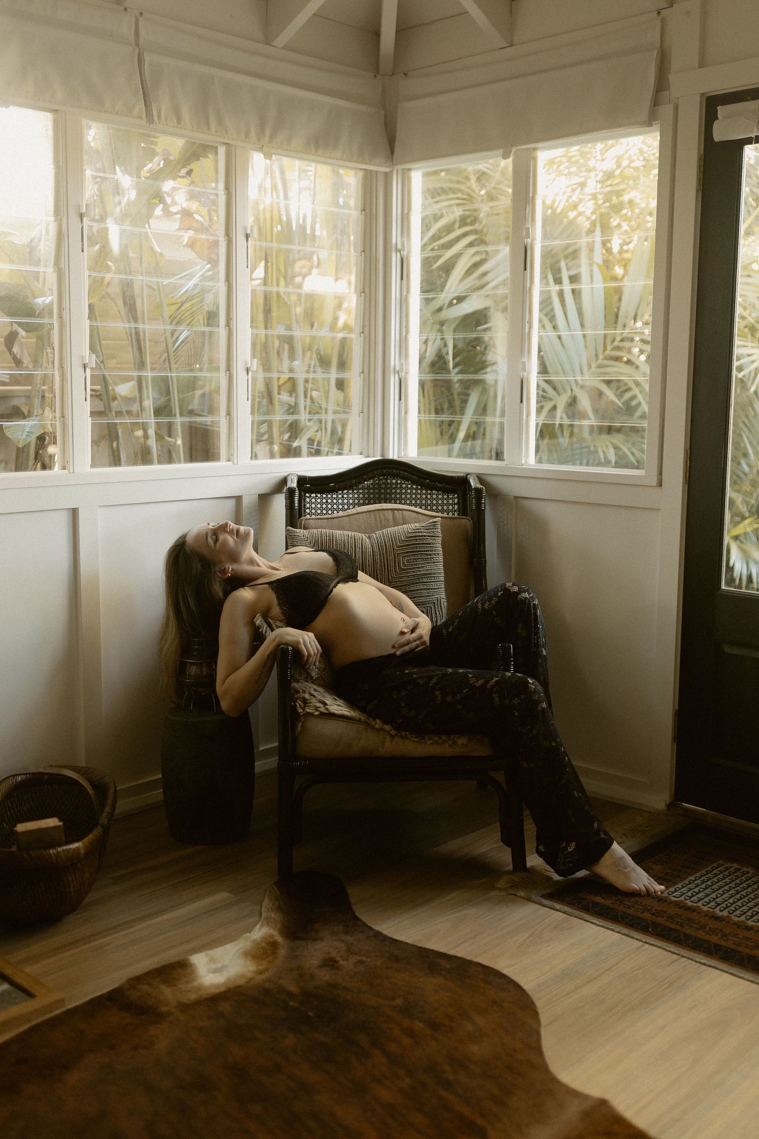 Artistic maternity photo in a bright sunroom with vintage furniture and wooden floors.