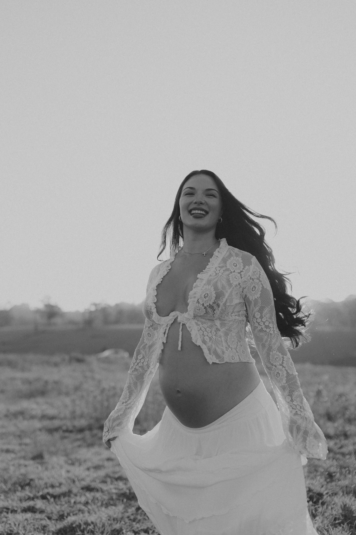Woman in white lace dress twirls joyfully in a field during a photoshoot.