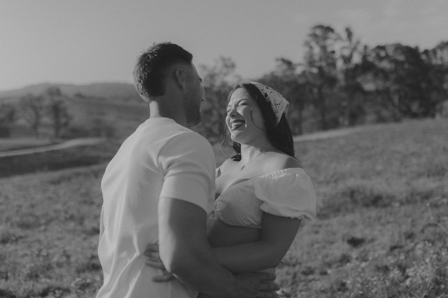 Romantic black and white portrait of couple embracing in countryside setting.