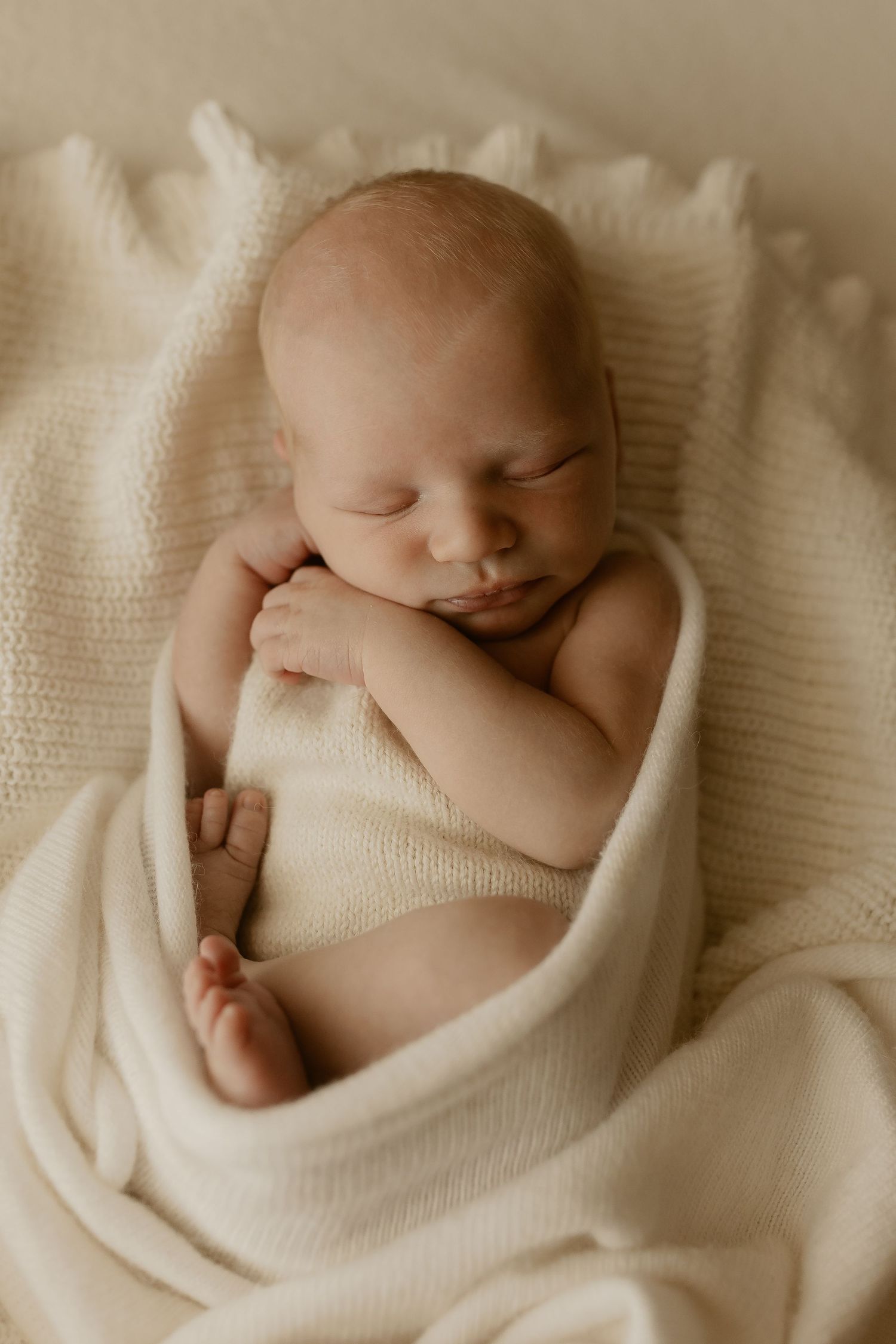 A newborn baby peacefully sleeping wrapped in soft white blankets in a serene black and white photo series.